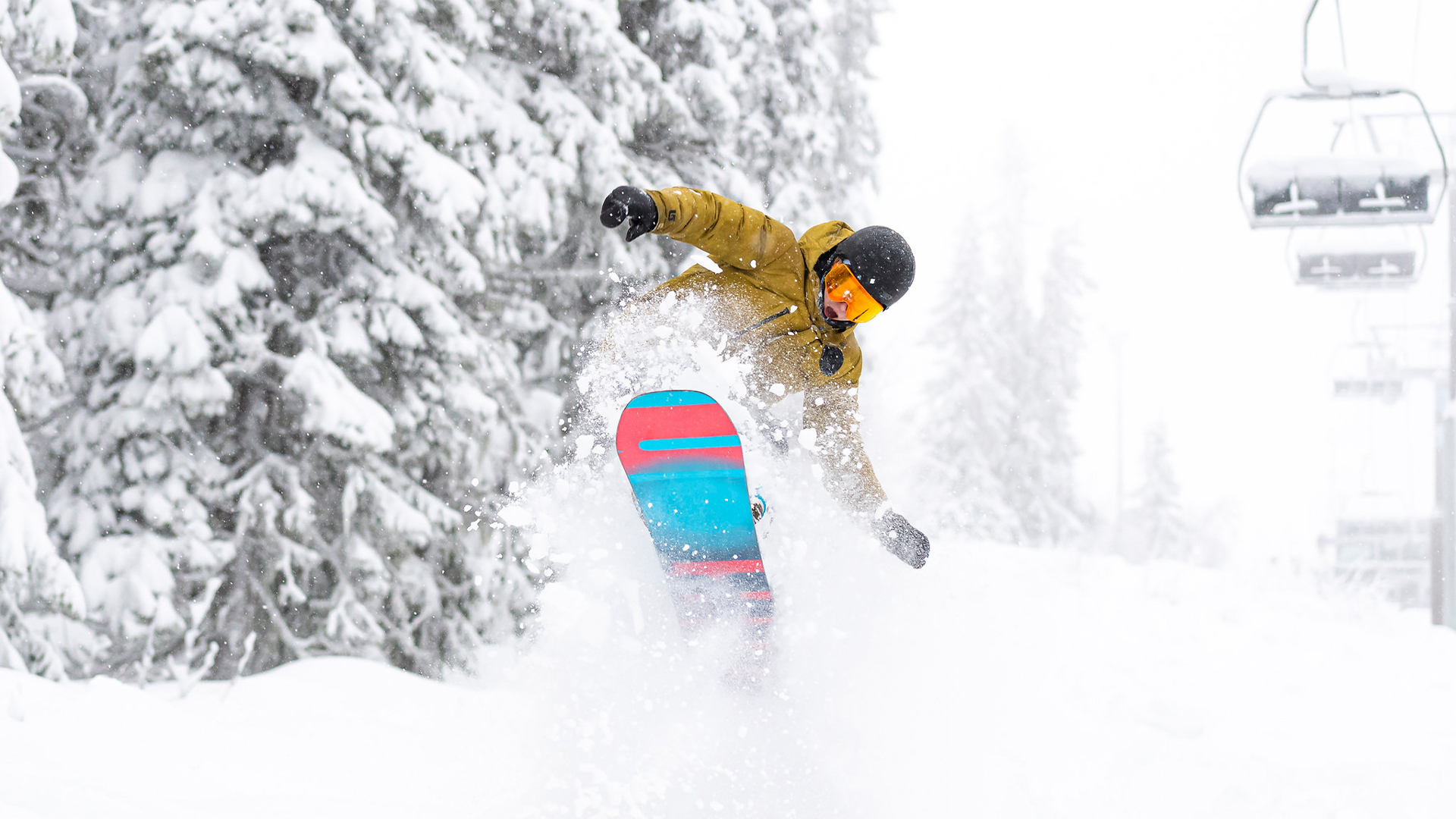 Snowboardåkare gör ett hopp i snöig skogsmiljö med färgstark bräda