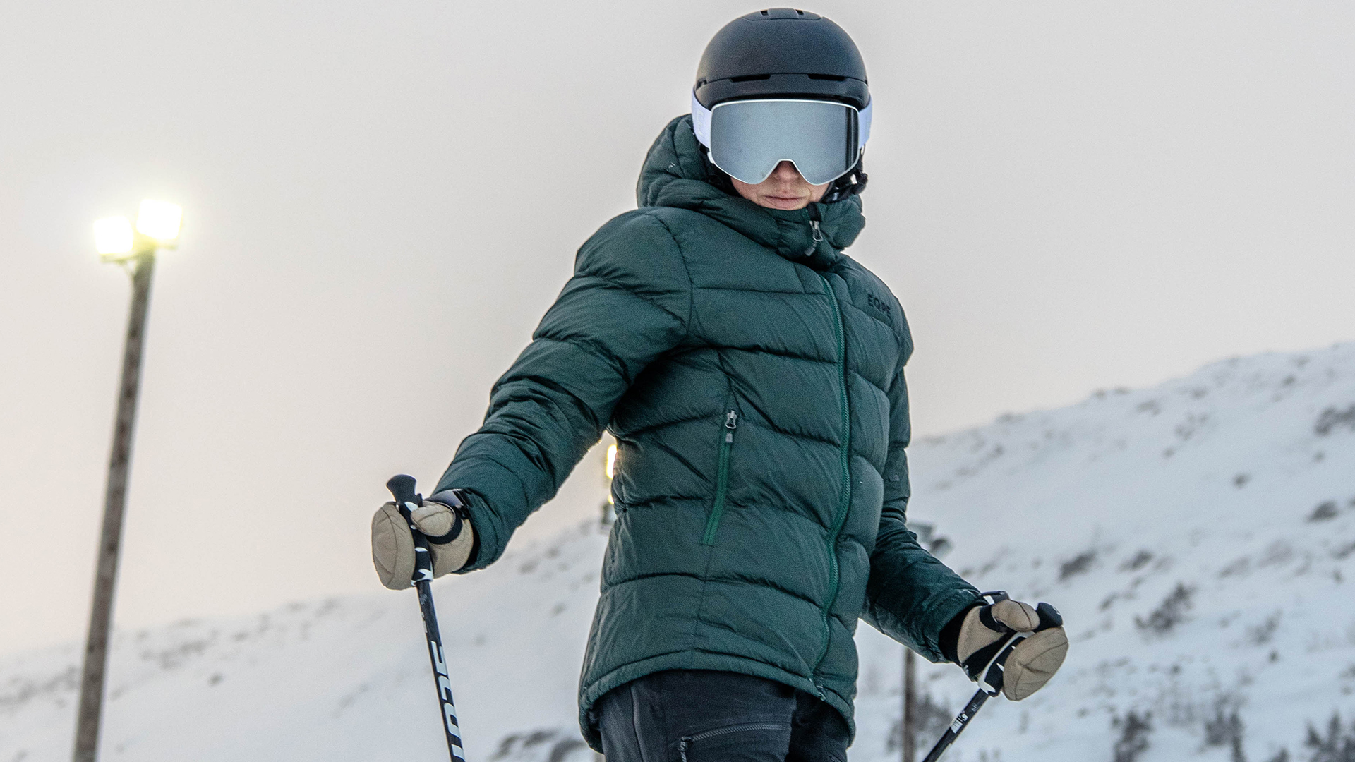 Person som åker skidor i vinterlandskap, iförd grön jacka och svart hjälm