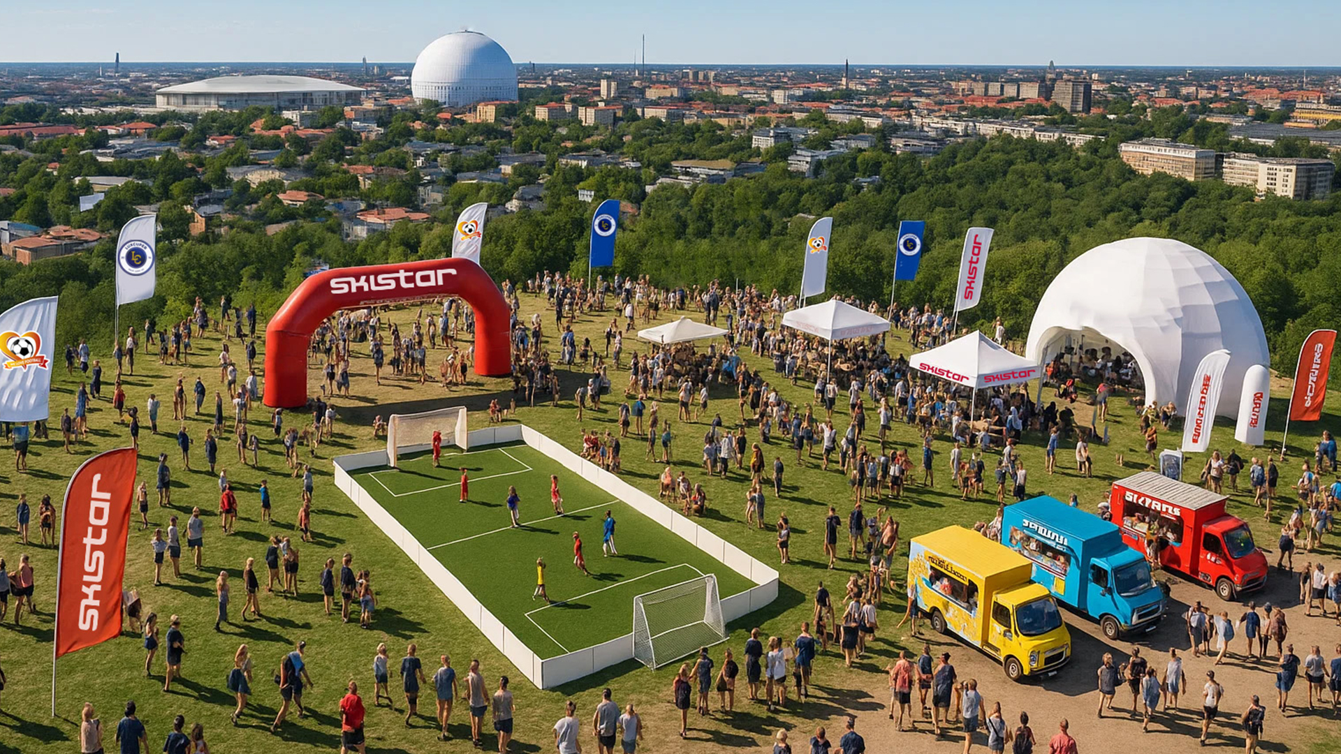 Festivalområde med grön gräsmatta och människor som deltar i utomhusevenemang. Små fotbollsplaner, foodtrucks och tält märkta med "SkiStar". Stockholms stadslandskap syns i bakgrunden