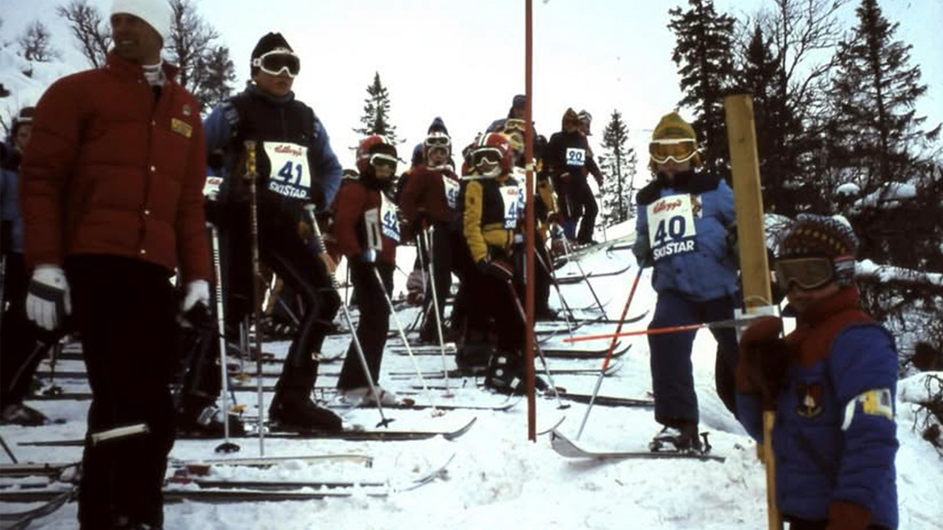 Skidåkare redo för start vid en tävling i ett snötäckt landskap med omgivande träd