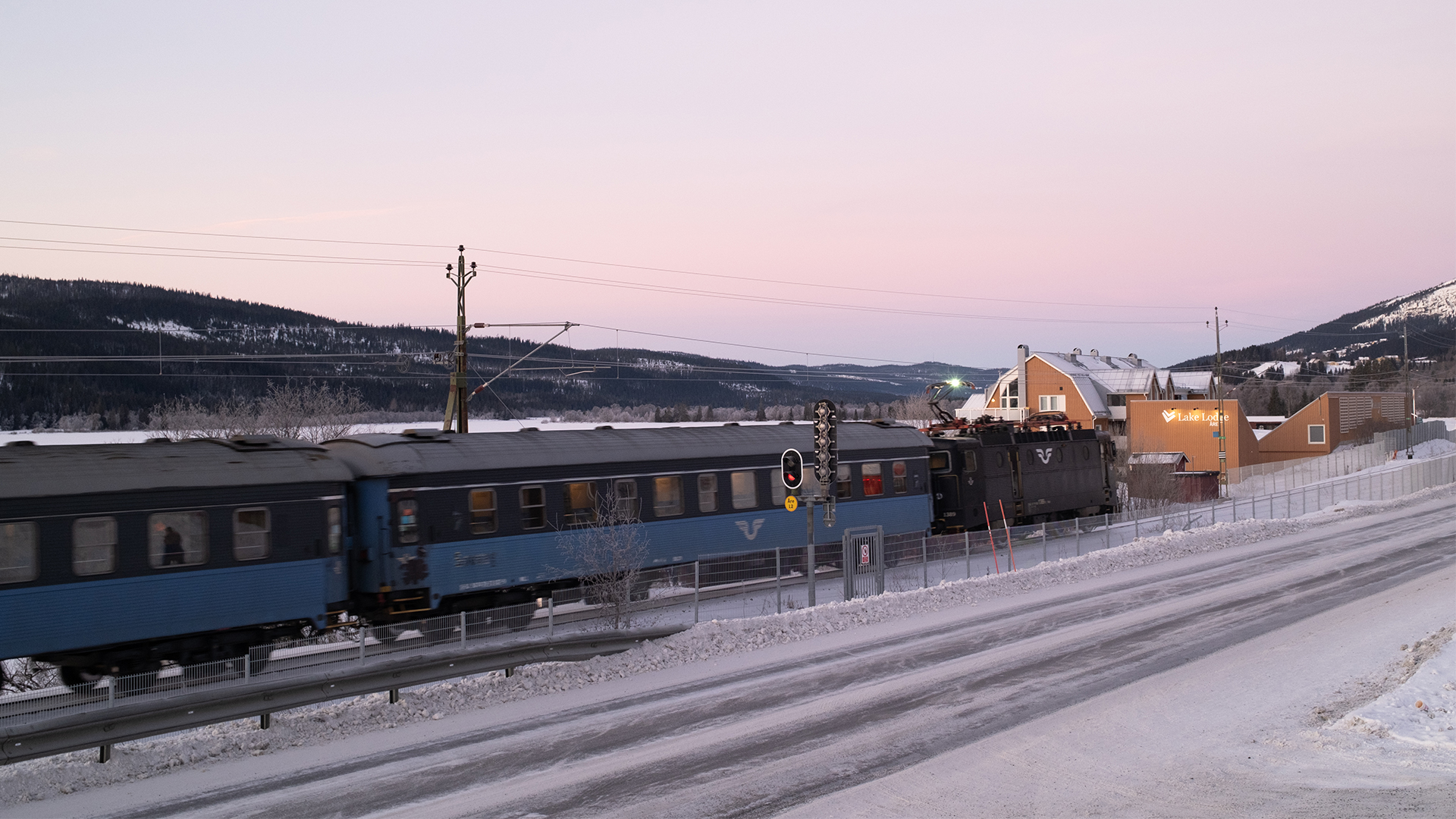 Tåg på vinterväg, snötäckta landskap och hus i bakgrunden i svensk landsbygd vid solnedgång
