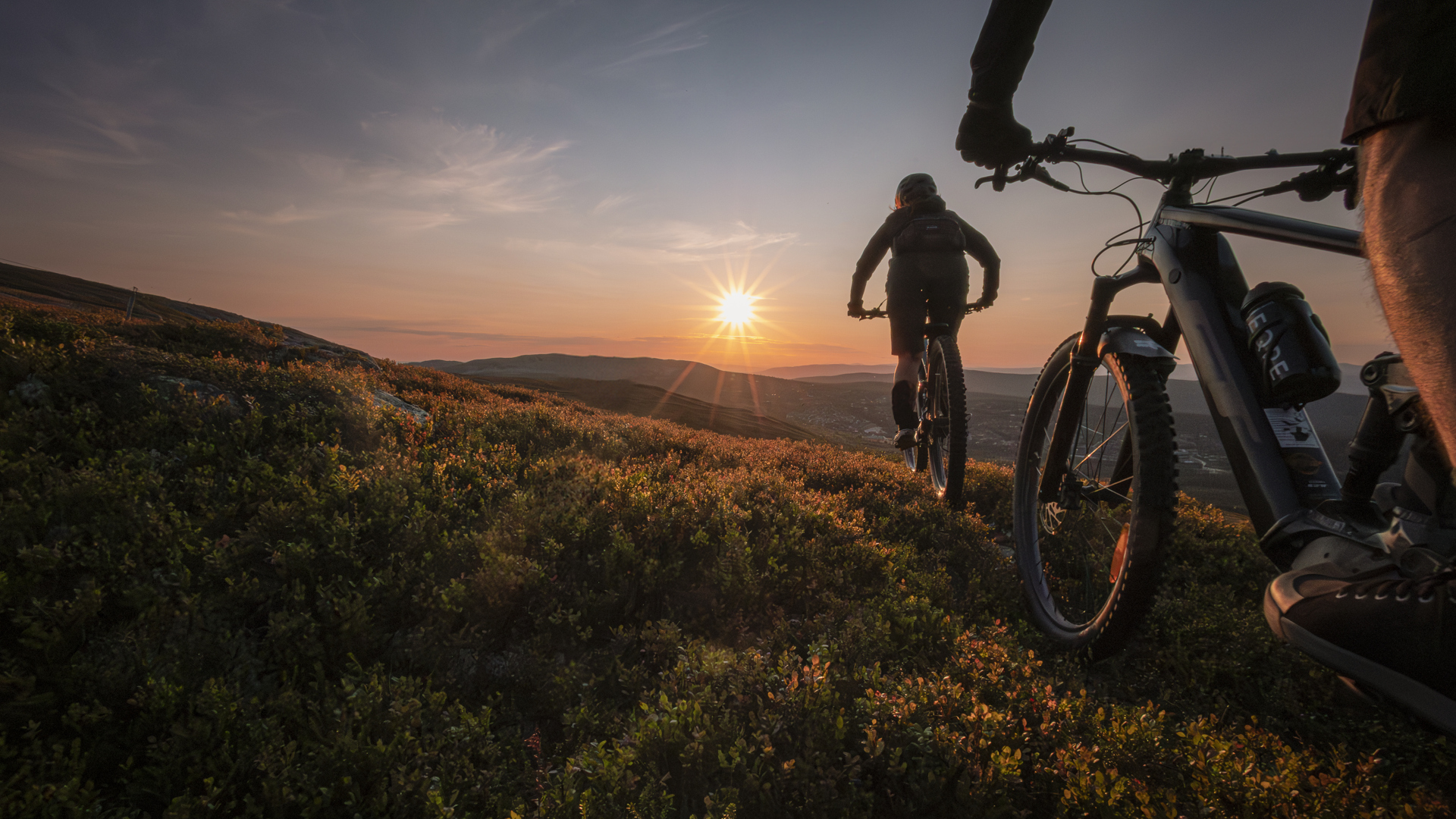 Cykling i bergen vid solnedgången, silhuetter av två cyklister med fantastisk utsikt över landskapet