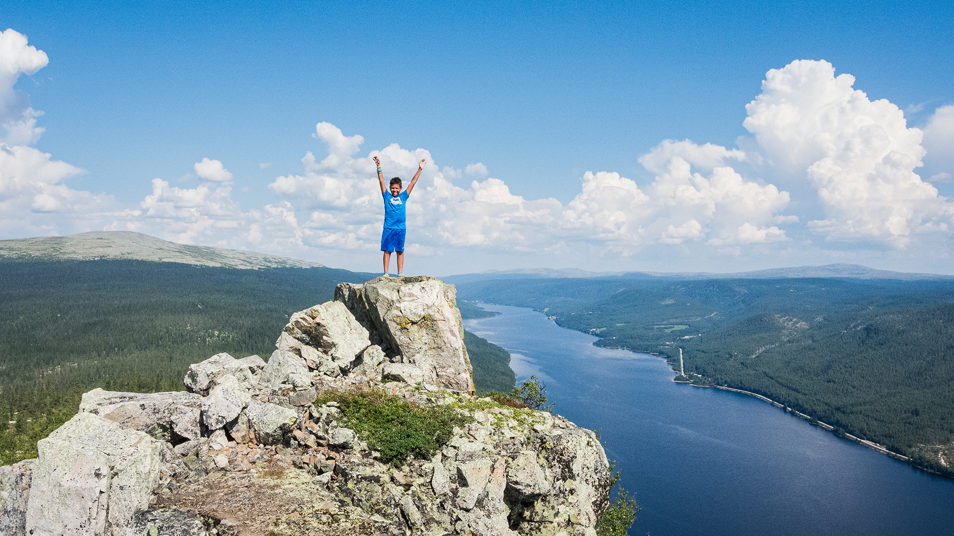 Person on a rock by a river in the forest under a clear blue sky