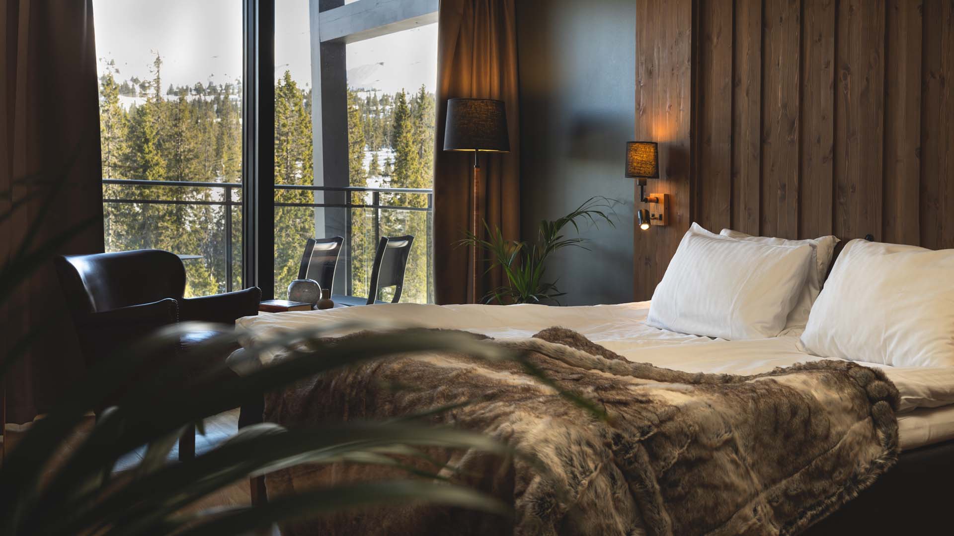 Lyxigt hotellrum med stor säng, mysiga filtar och utsikt över skog och snöklädda landskap genom stora fönster