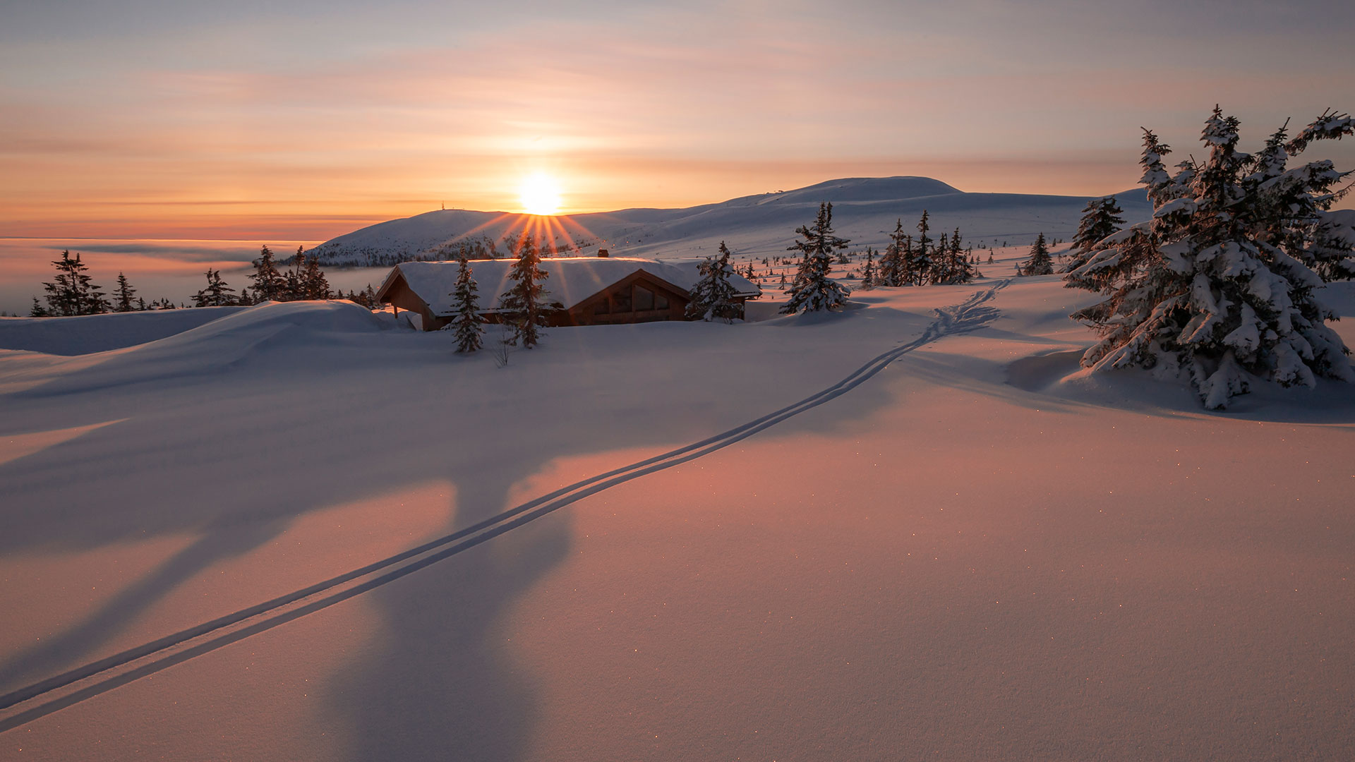 Solnedgång över snötäckt landskap i fjällen med skidspår och en stuga i bakgrunden i Sverige