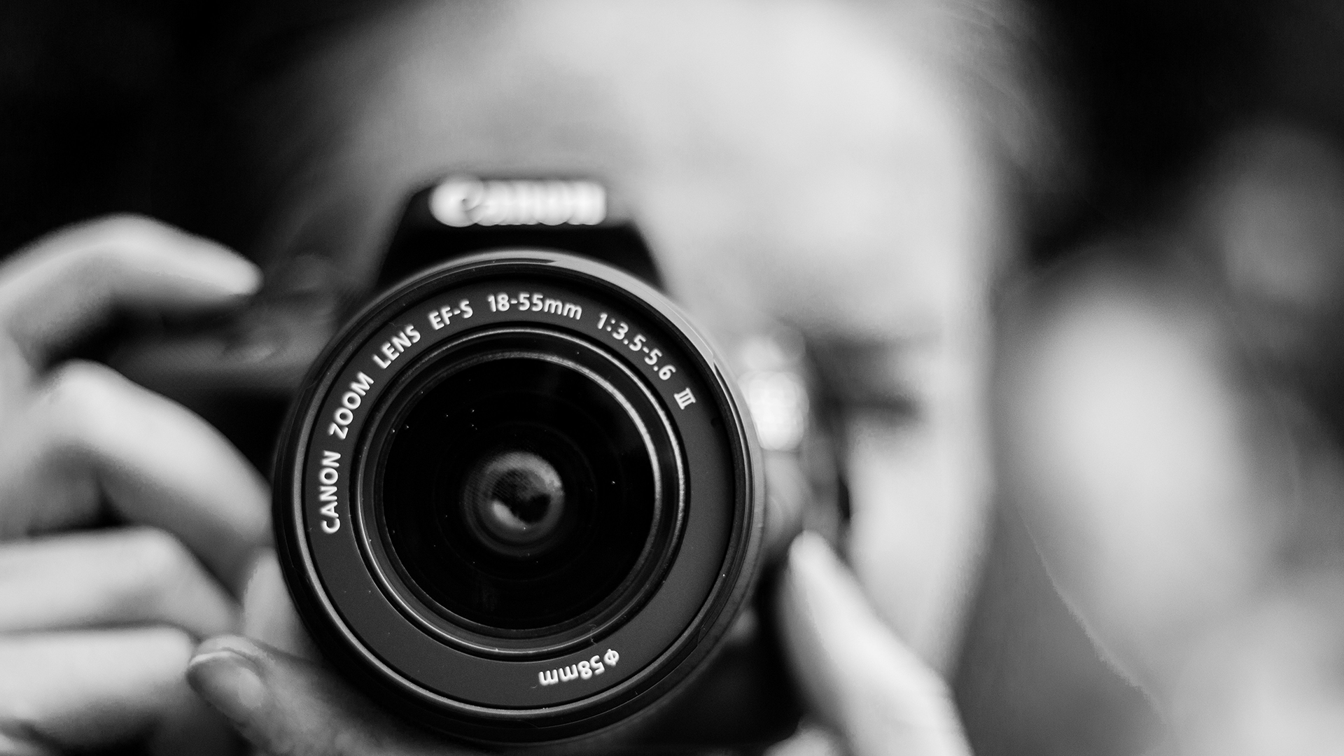 Person håller en kamera med Canon-objektiv i fokus, svartvit bild