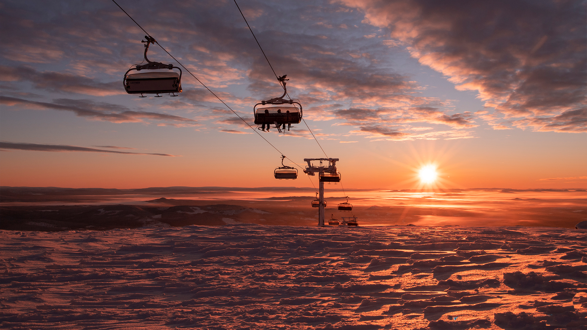 Solnedgång över ett snötäckt berg med skidliftar i silhuett mot en färgglad himmel i Trysil