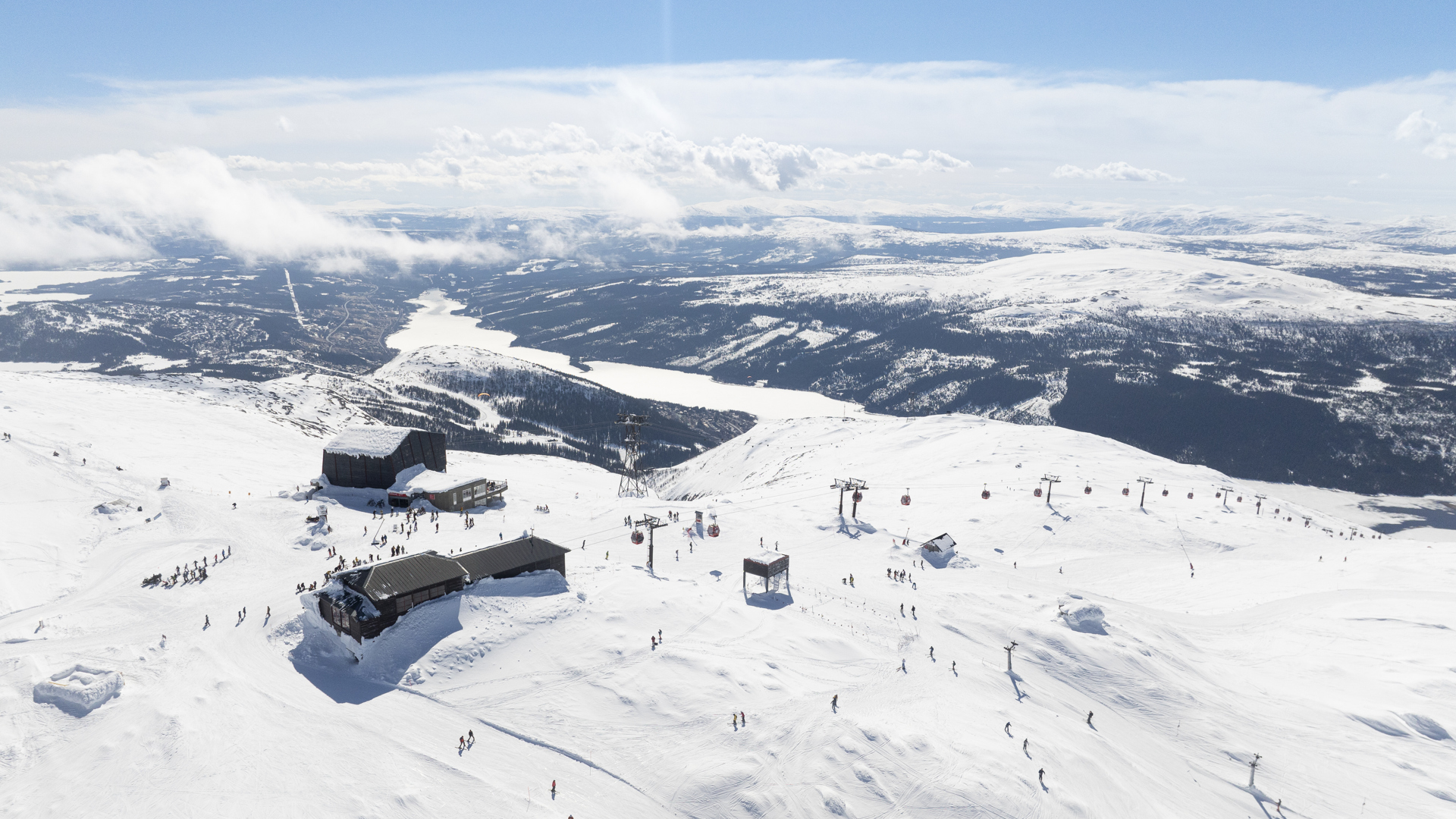 Vinterlandskap i Åre med skidåkare och liftar på snötäckta berg under en klarblå himmel