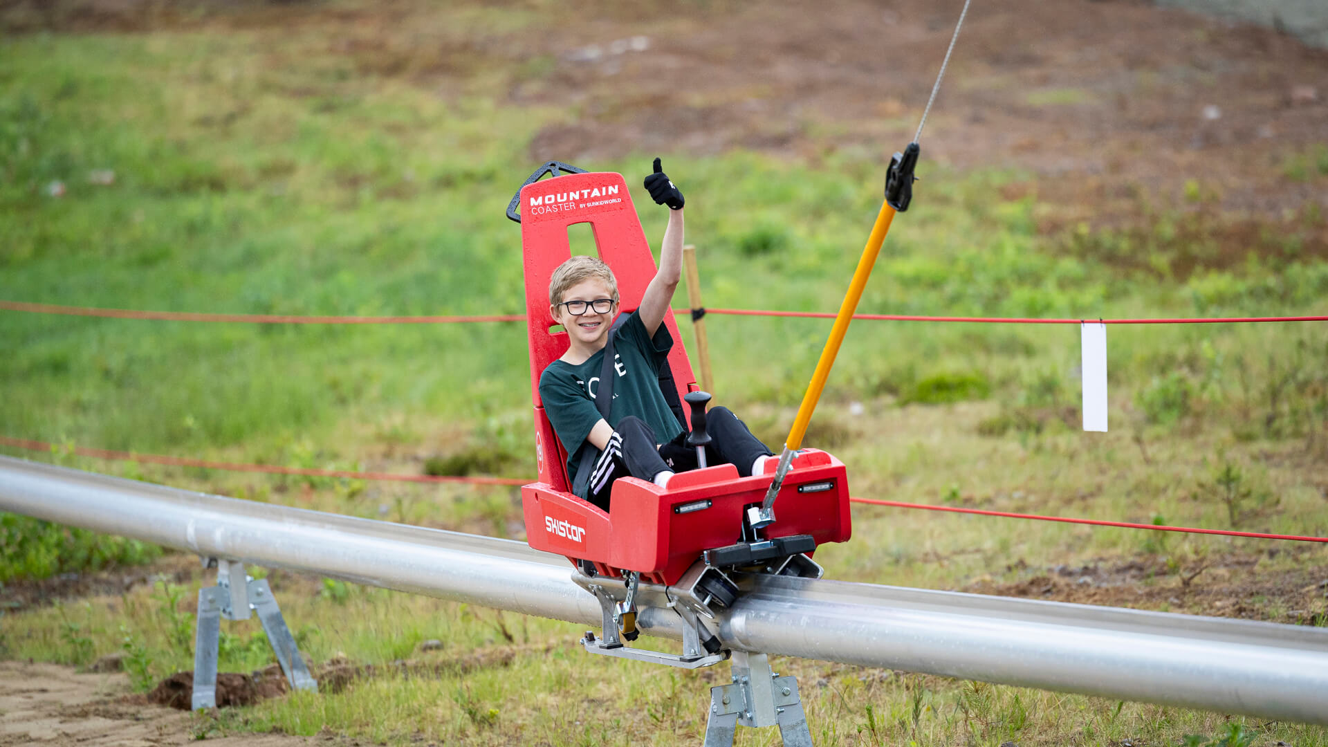 Ung person åker Mountain Coaster, en typ av rodel, i Trysil i fjällmiljö, visar glädje med tummen upp