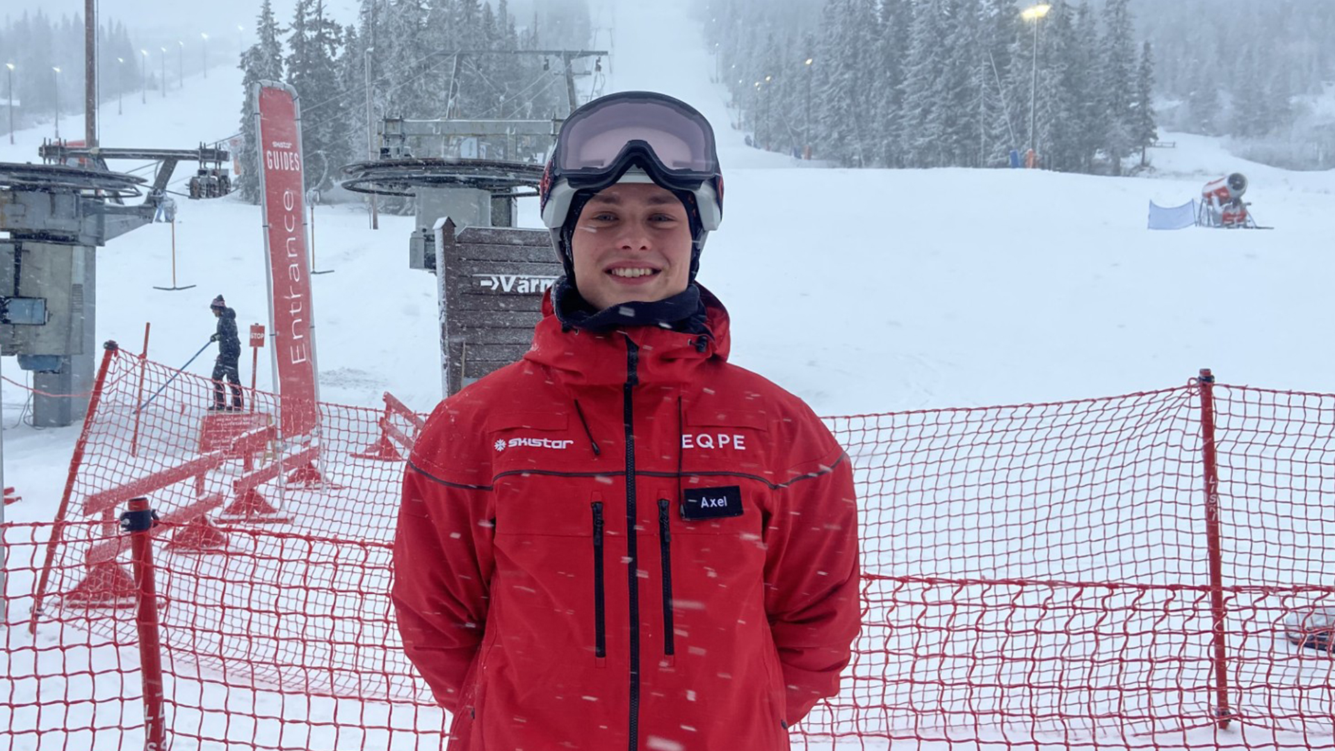 Person i röd jacka står vid skidbacke med snöfall i bakgrunden i skidort