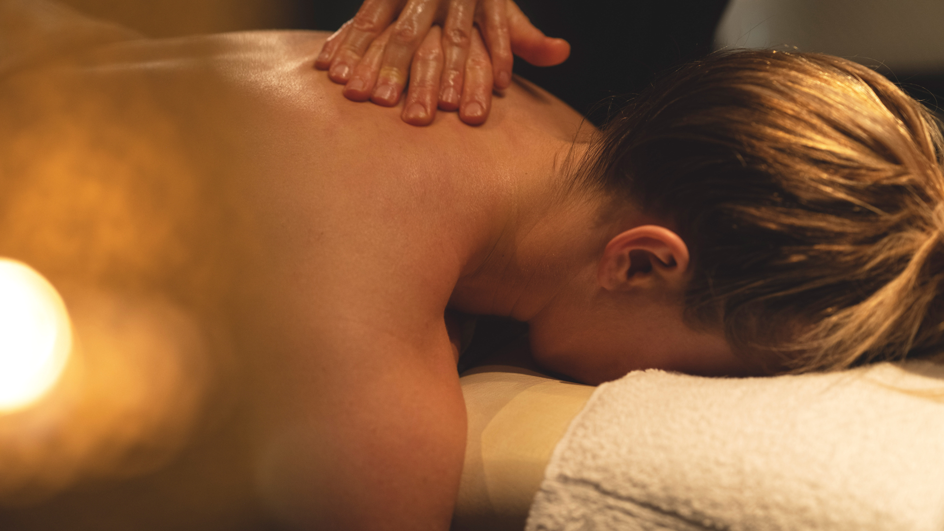 Person får avslappnande massage på ryggen i ett spa, med mjuk belysning och lugnande atmosfär