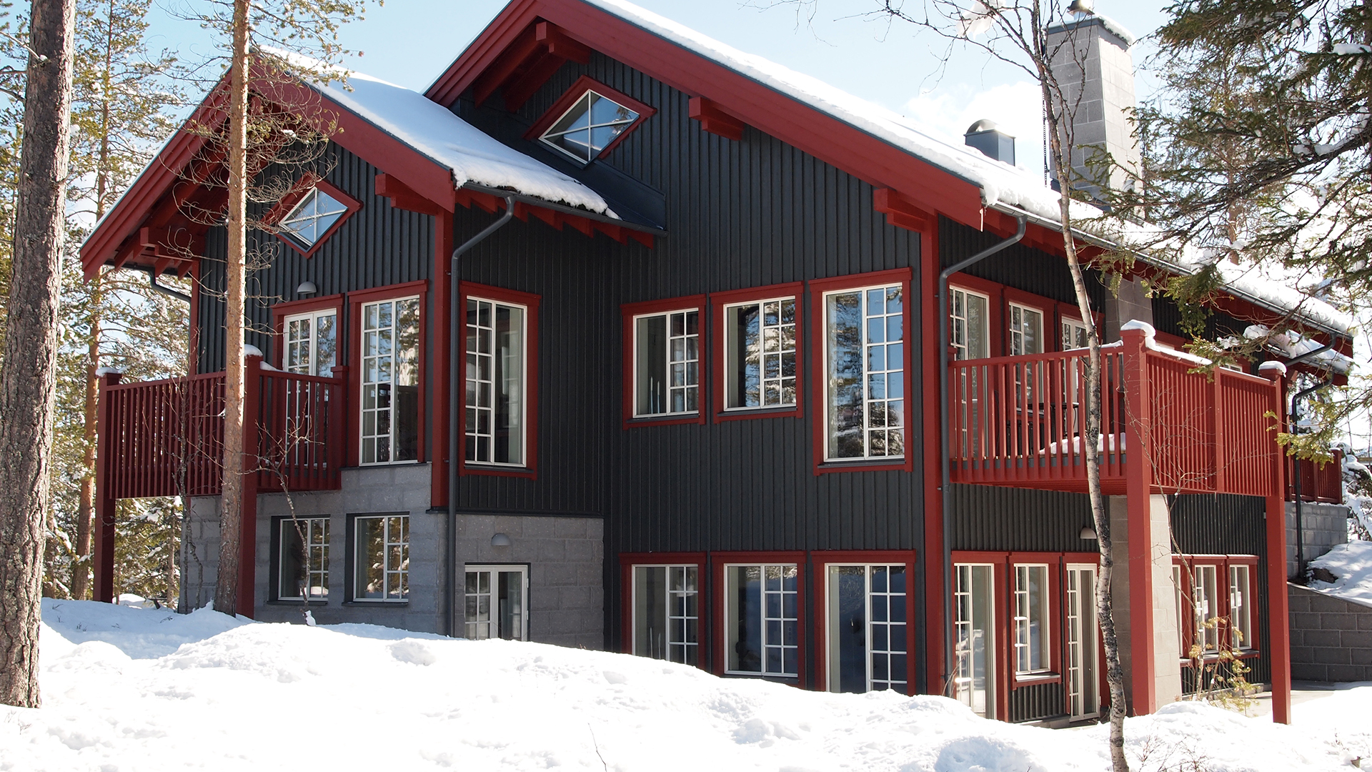 Svart-rött trähus i snöig skogsmiljö under vintern