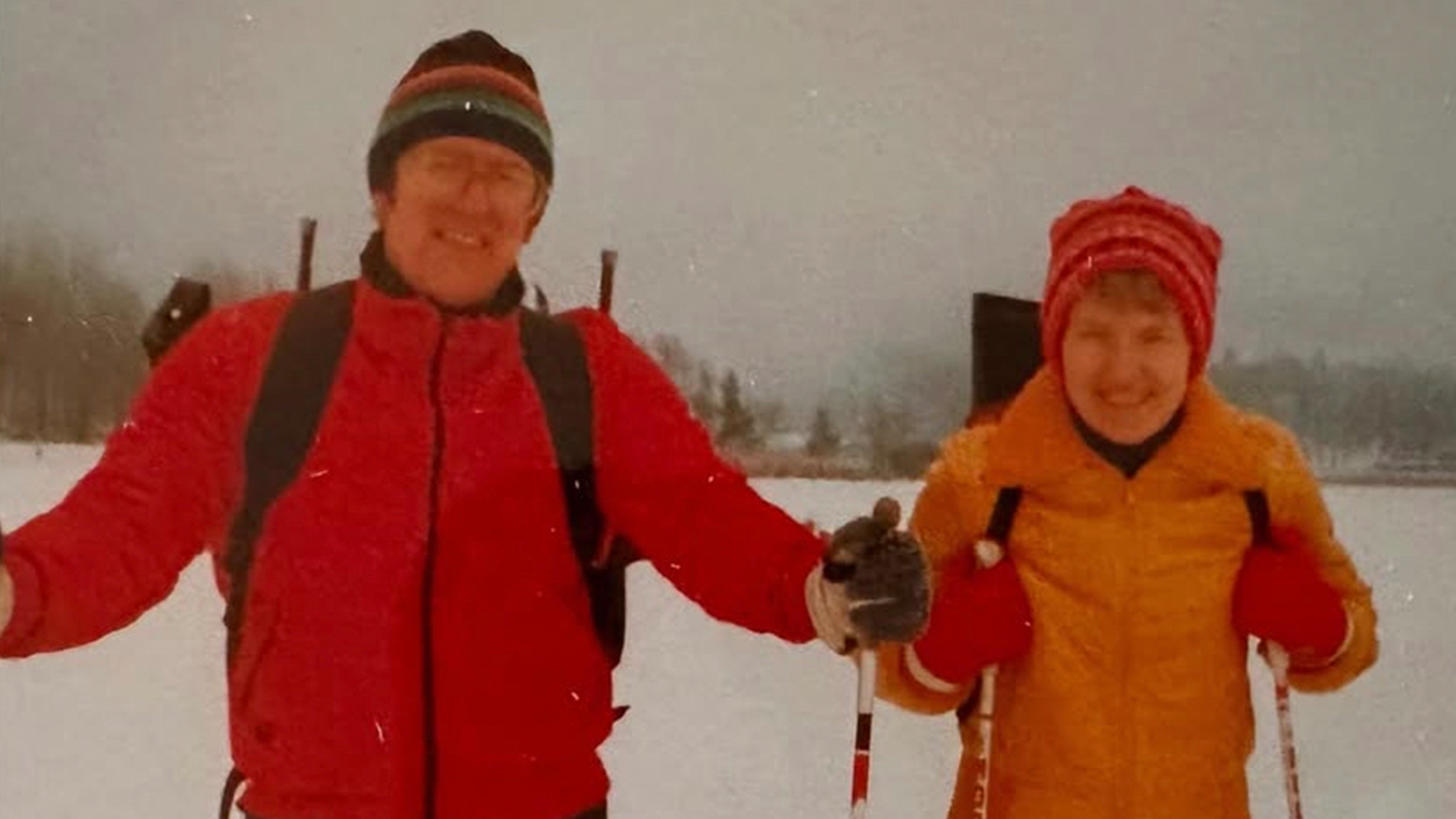 Två personer klädda i färgglada vinterkläder och mössor som åker längdskidor på ett snötäckt landskap
