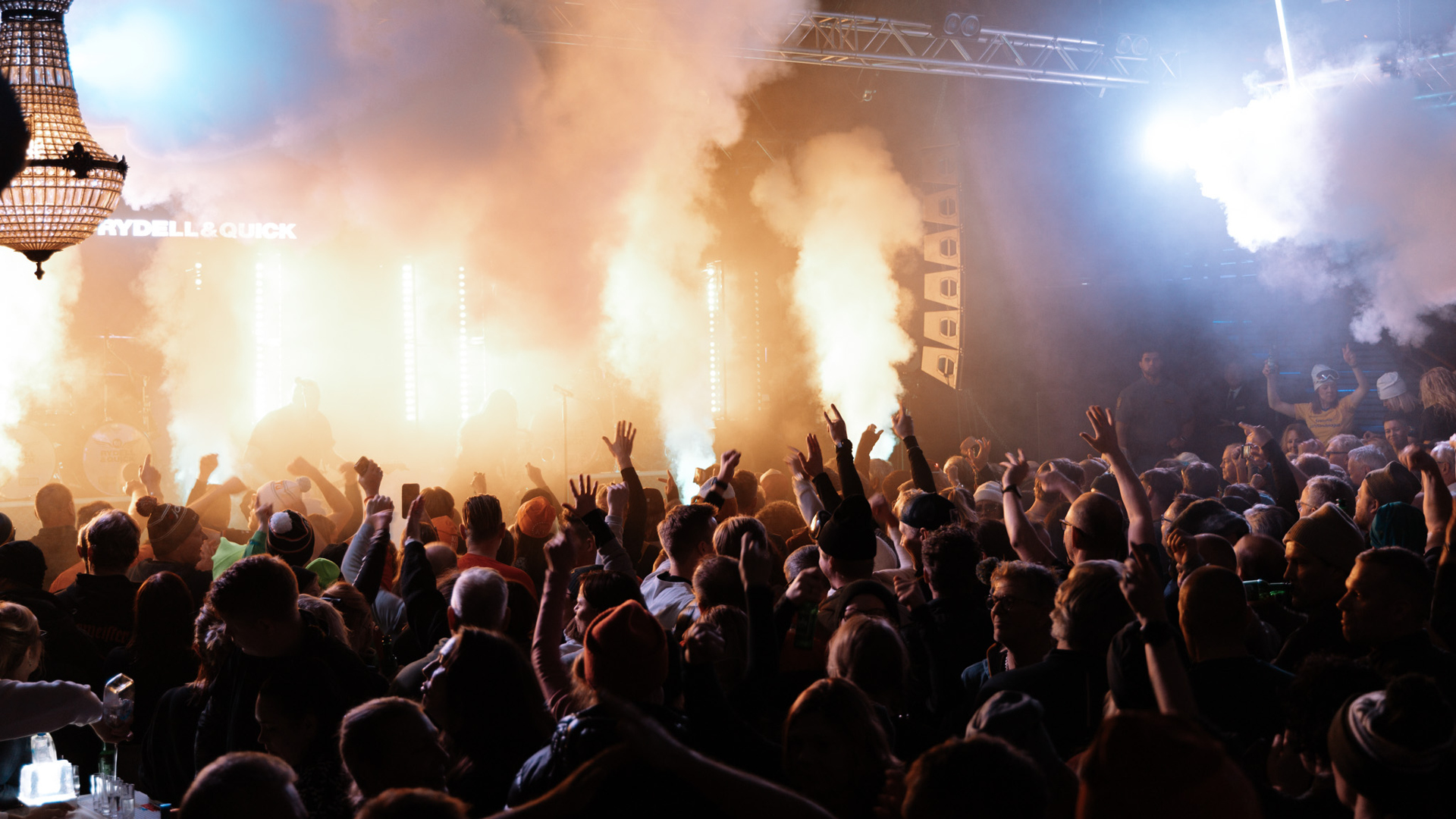 Konsertpublik som höjer händerna medan rök och ljus fyller scenen