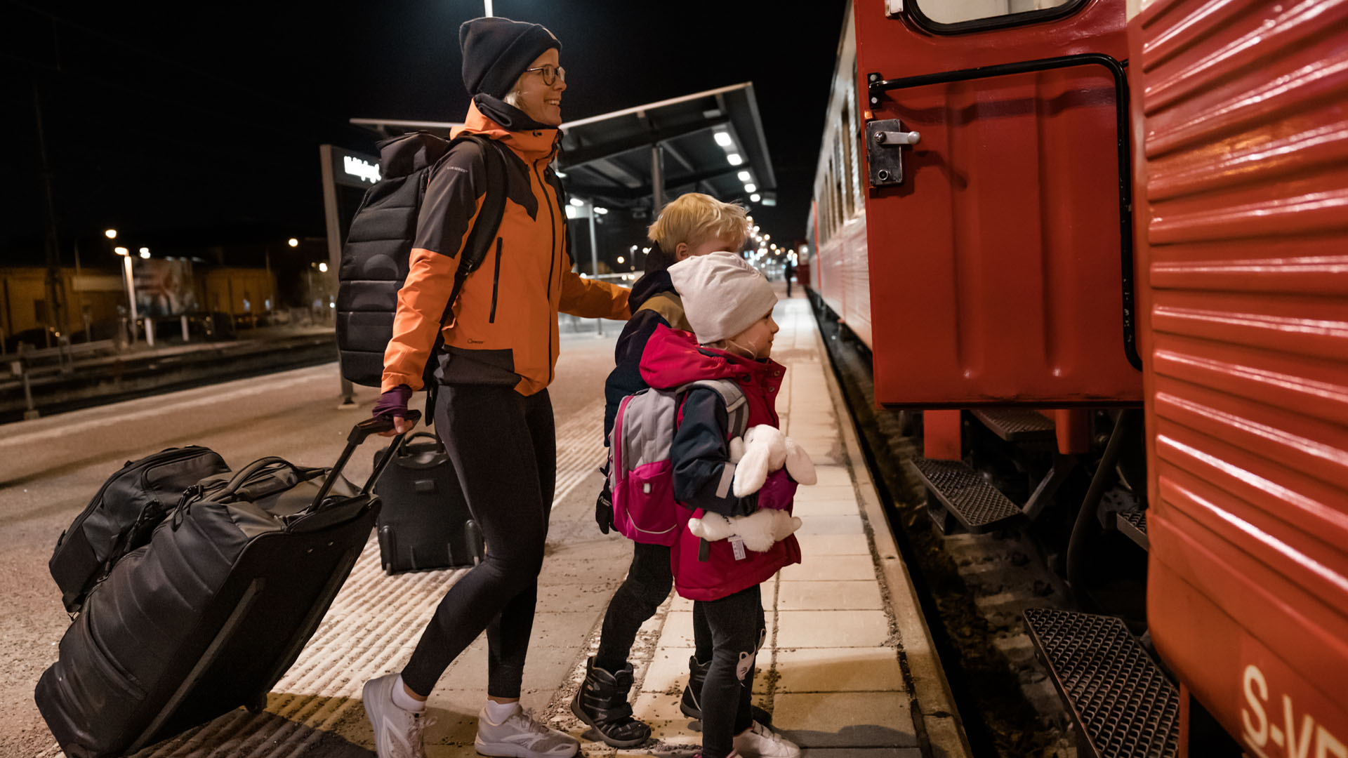 Familj går ombord på nattåg med bagage på station i Sverige, kvällstid