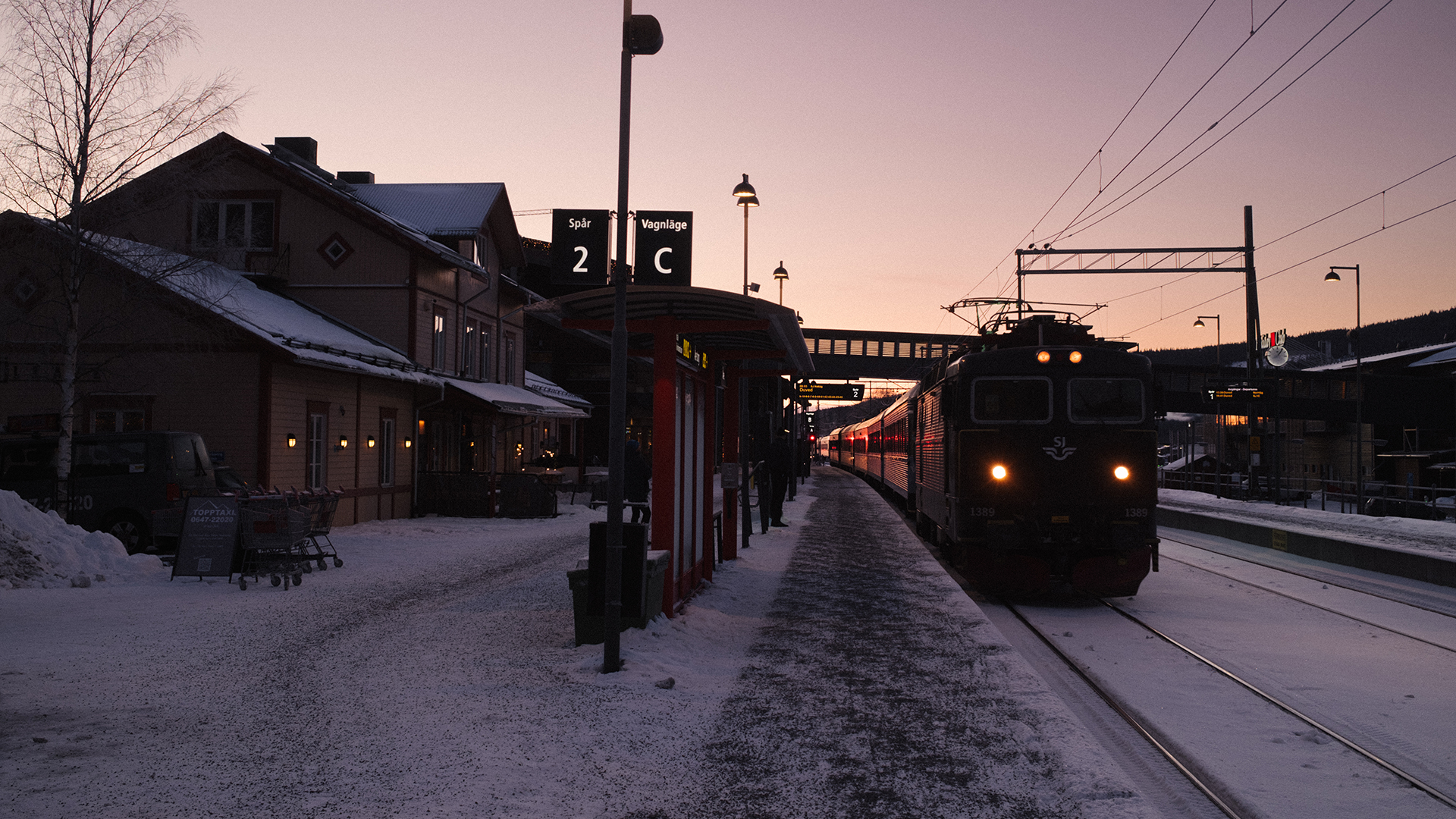 Tåg anländer till en snöig järnvägsstation i Sverige vid solnedgång, spår 2C