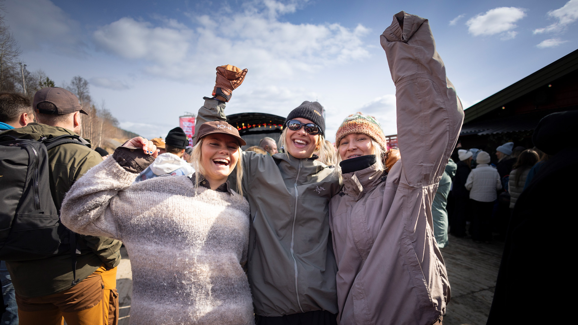 Tre glada personer firar utomhus på en musikfestival under en solig dag i Sverige