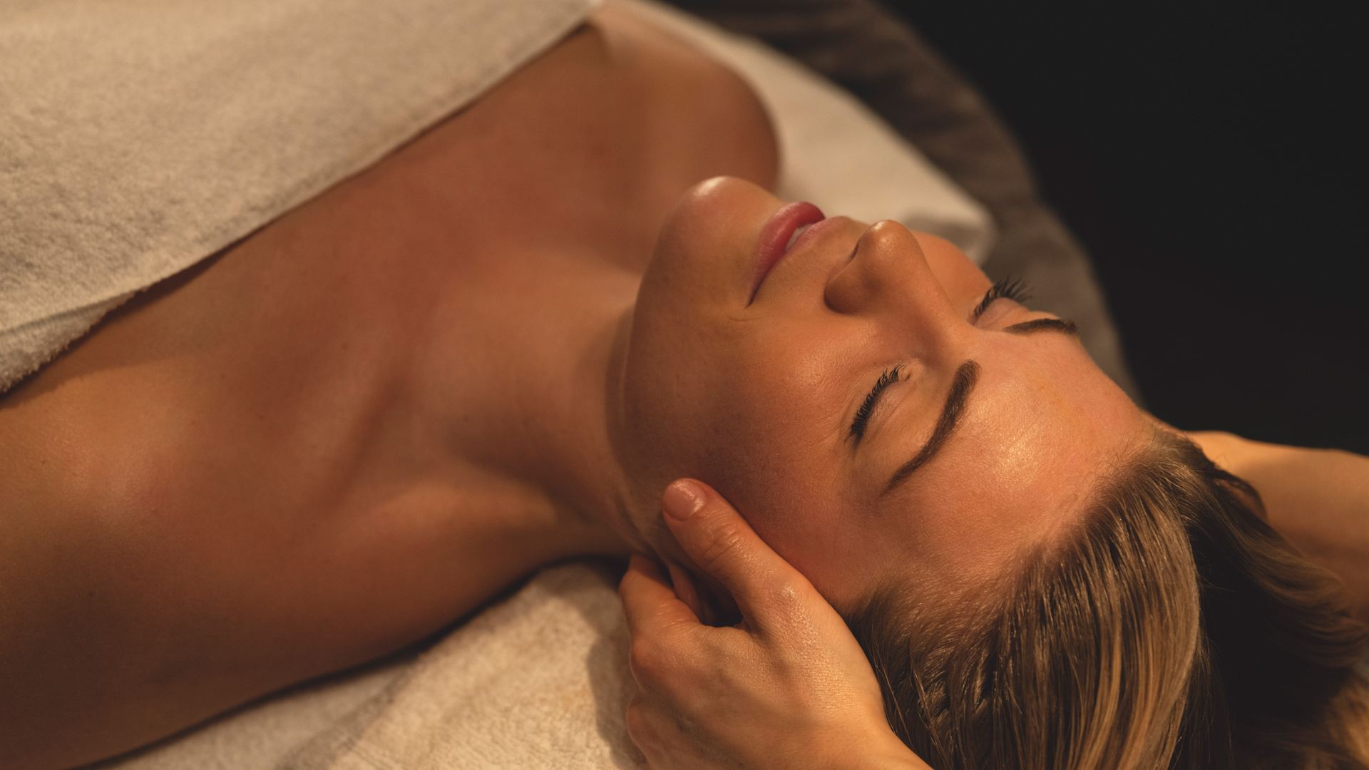 Kvinna får avslappnande ansiktsmassage på spa, insvept i en vit handduk, med fokus på avslappning och välbefinnande