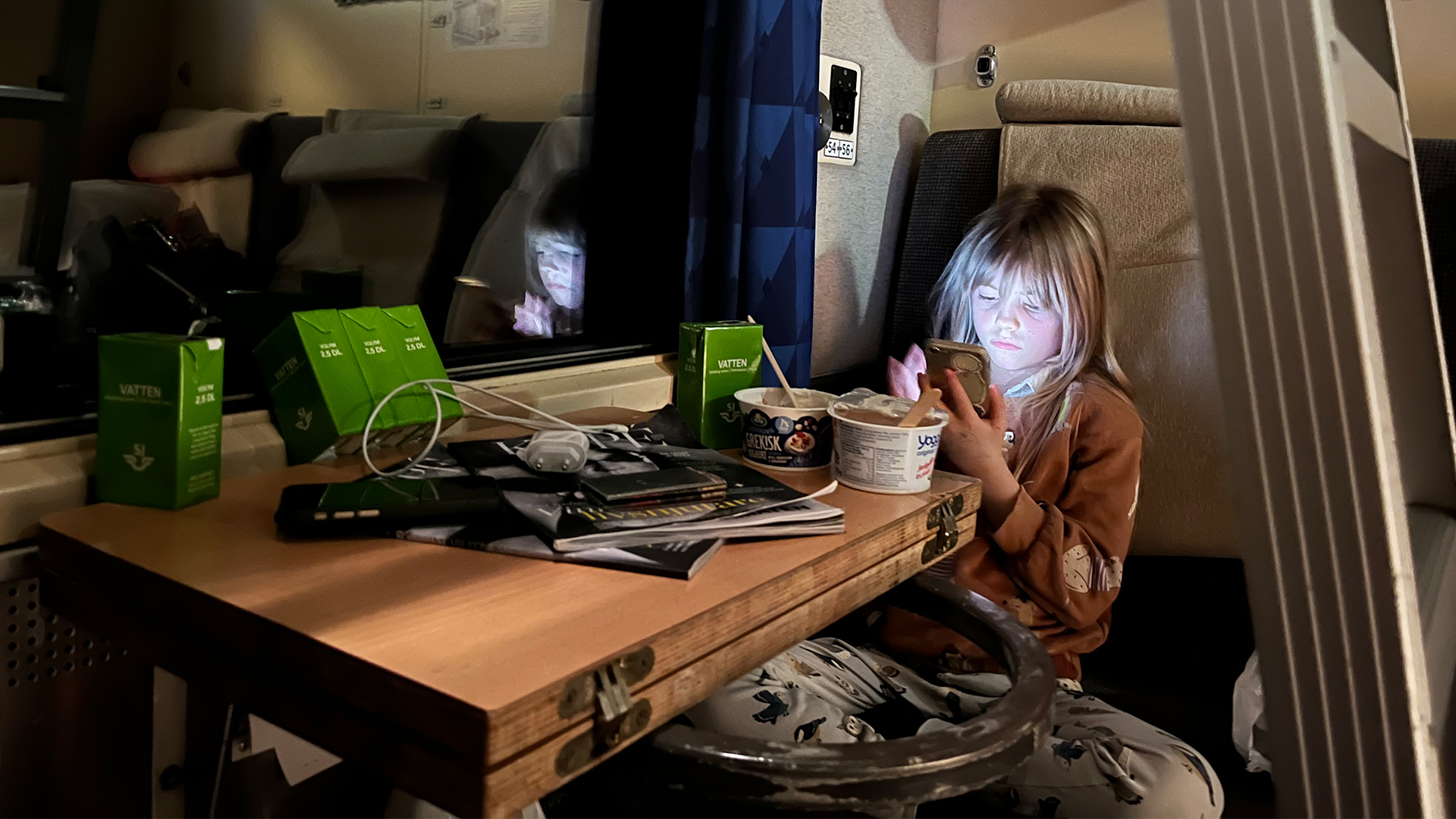 Barn i tågkupé med telefon, mat och dryck på bordet