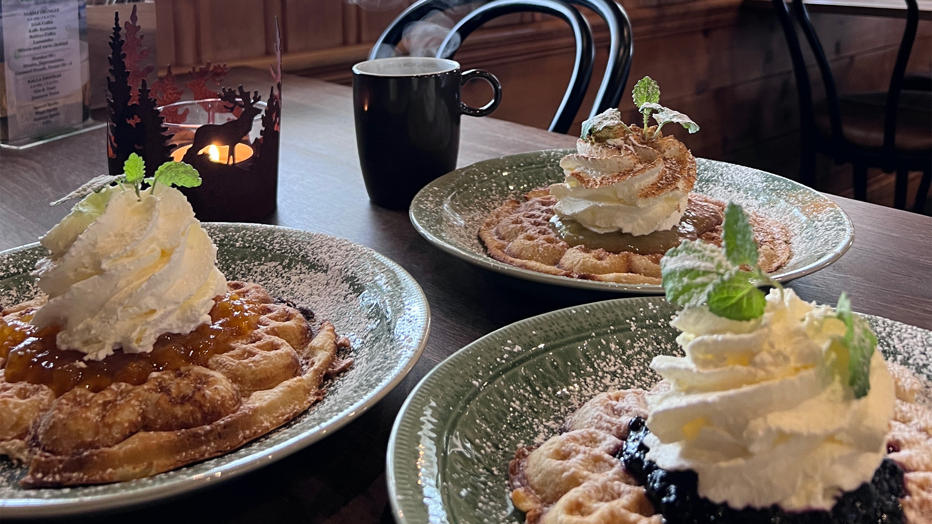 Tre nygräddade våfflor toppade med grädde, sylt och myntablad på tallrikar i ett mysigt café