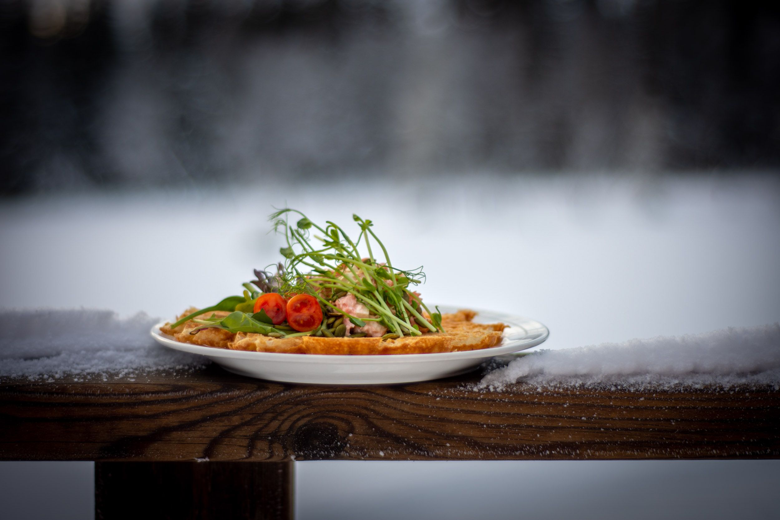 Tallrik med mat på träbord utomhus, dekorerad med sallad och körsbärstomater, med snötäckt bakgrund
