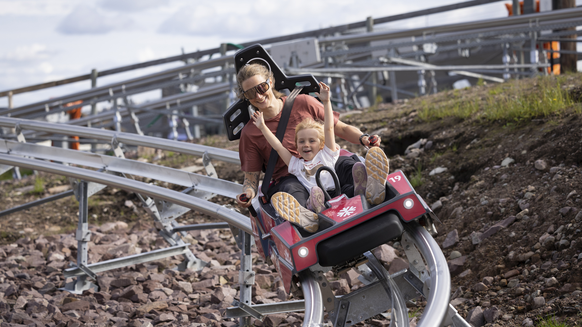 Mamma och dotter åker en berg- och dalbana utomhus med glädje och spänning i vackert landskap