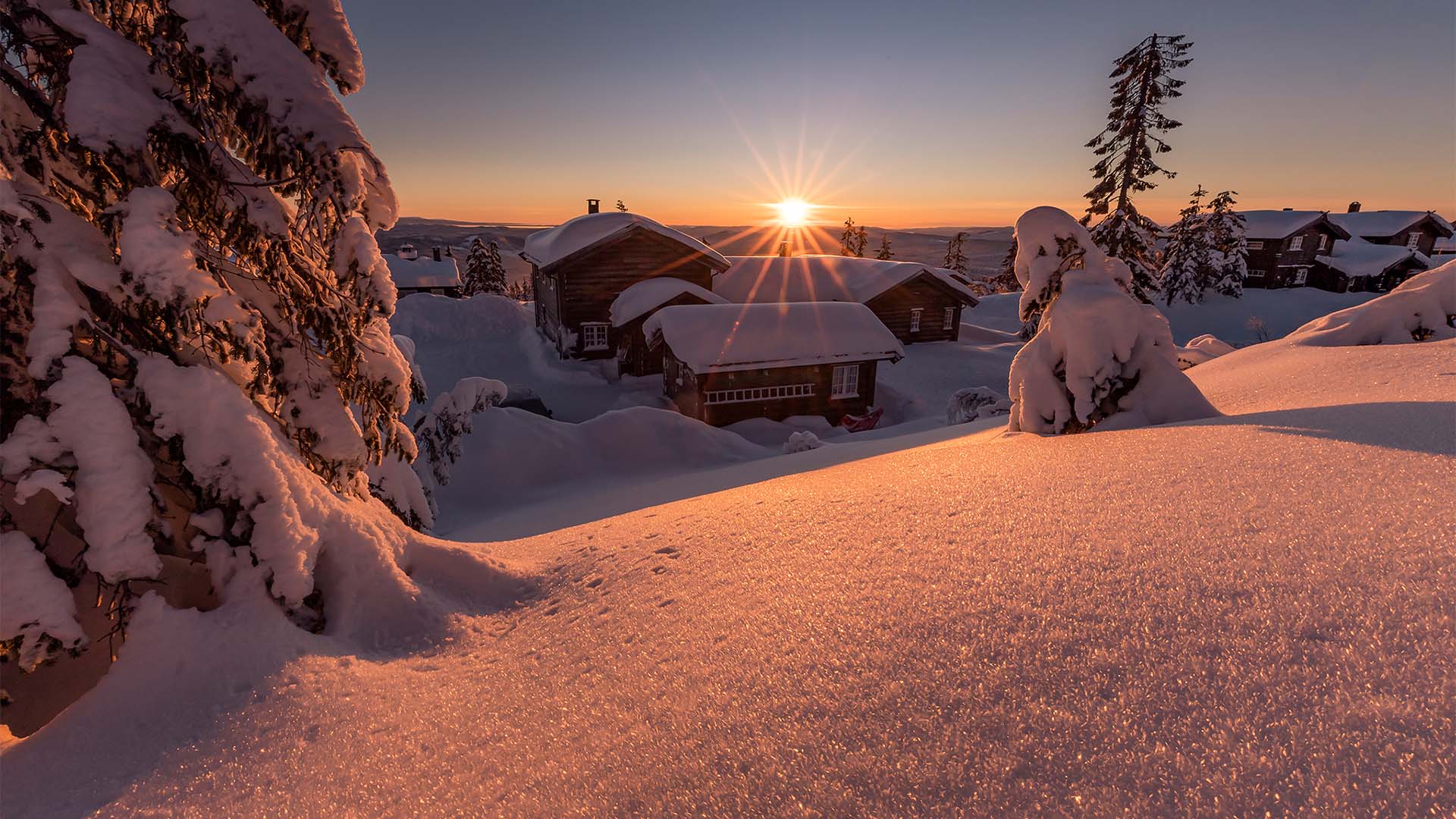 Soluppgång över snötäckta stugor och träd i ett vinterlandskap