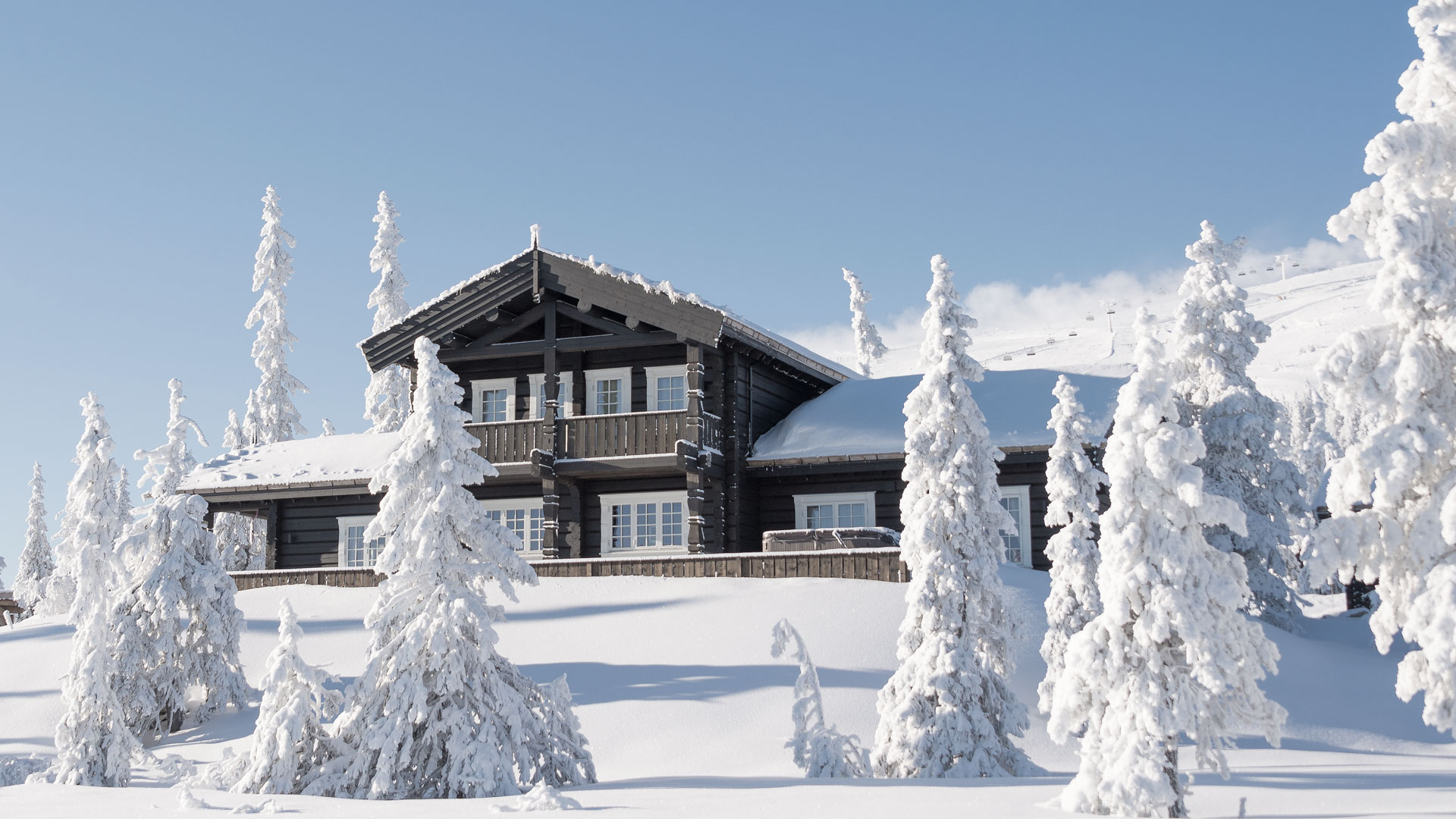 Häuser aus Holz in einer schneebedeckten Winterlandschaft mit schneebedeckten Tannen ringsum, blauer Himmel im Hintergrund