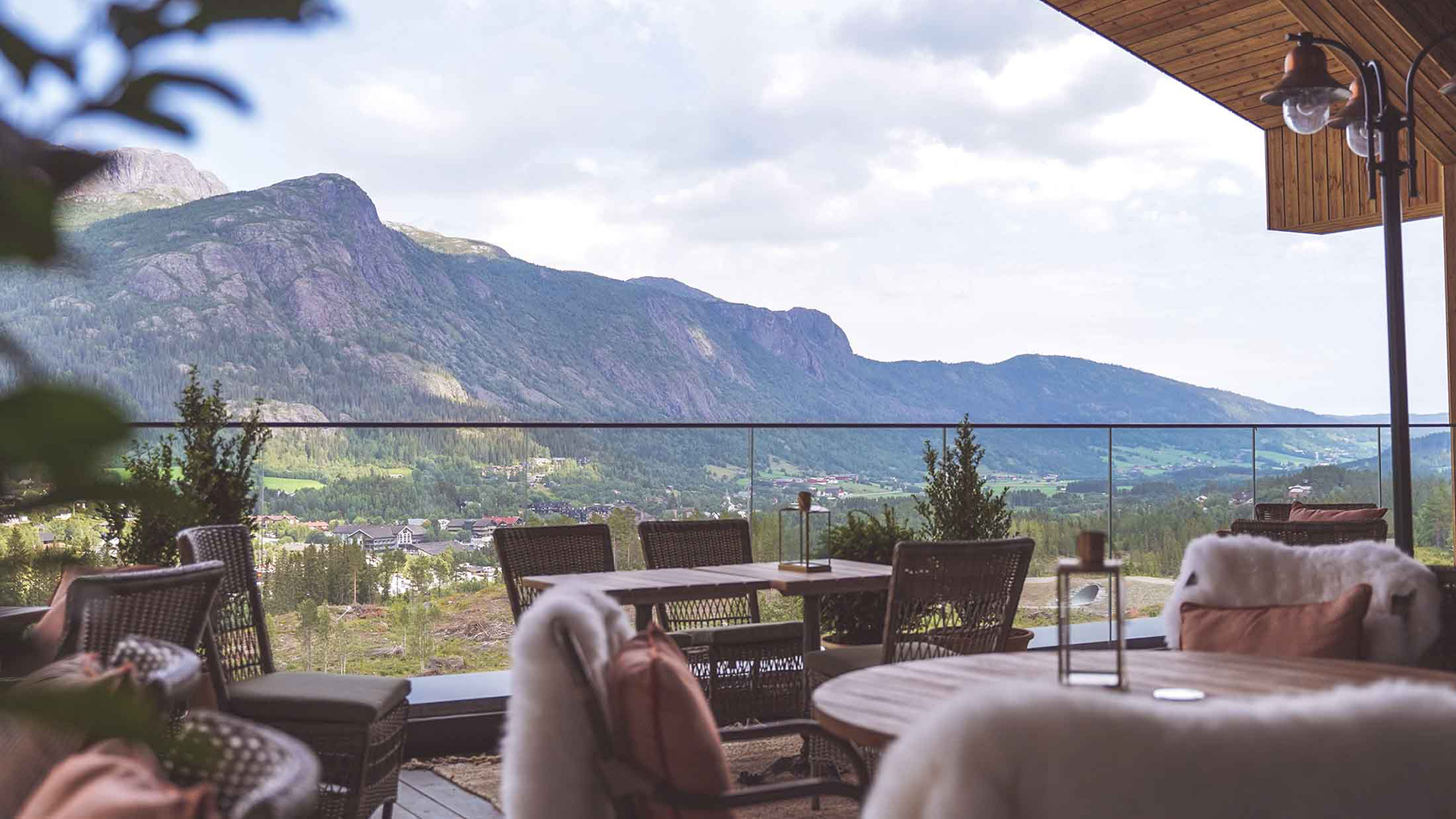 Utsikt över berg och dalgång från en modern terrass med bekväma sittplatser och glasräcke. Perfekt destination för avkopplande semester