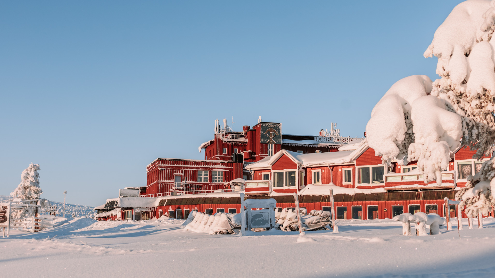 Röd hotellbyggnad täckt av snö i vintrigt landskap, under klarblå himmel