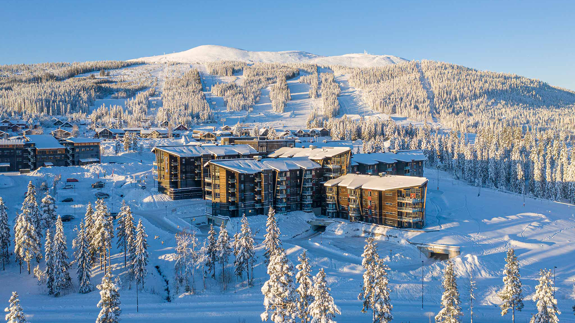 Fjälllandskap med snötäckta träd och modernhotell vid en skidort, vacker vinterdag