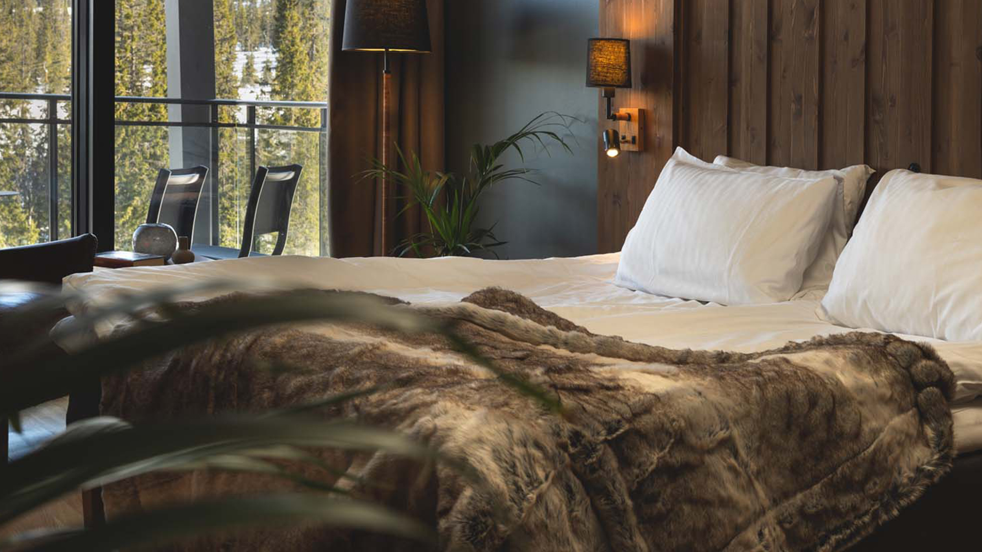 Lyxigt hotellrum med stor säng, pälsöverkast och fönster med utsikt över skog
