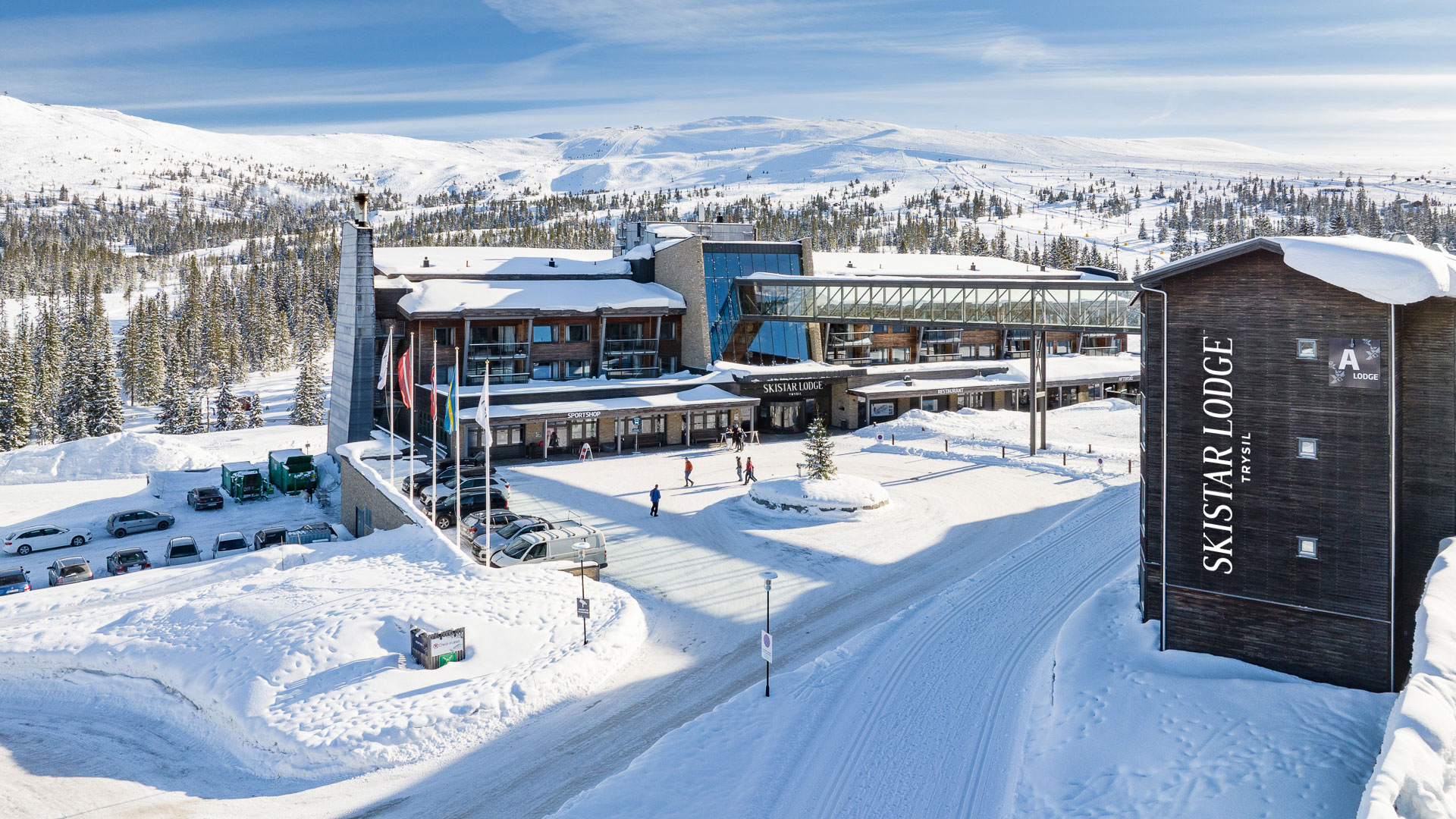 Skistar Lodge Trysil omgiven av snö och bergslandskap, med skidåkare och bilar i den snötäckta parkeringsplatsen
