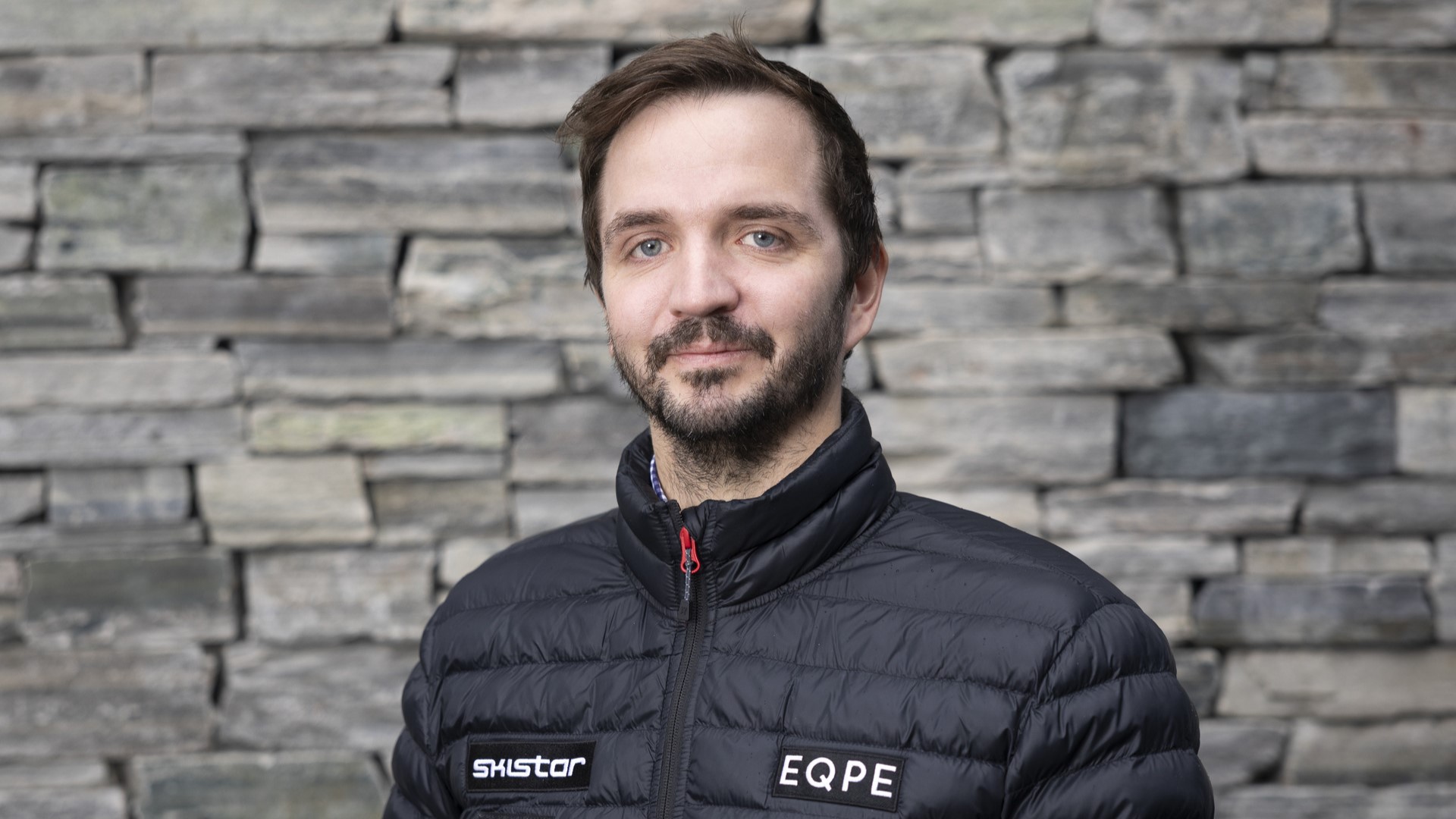 Mann i svart dunjakke foran en steinmur