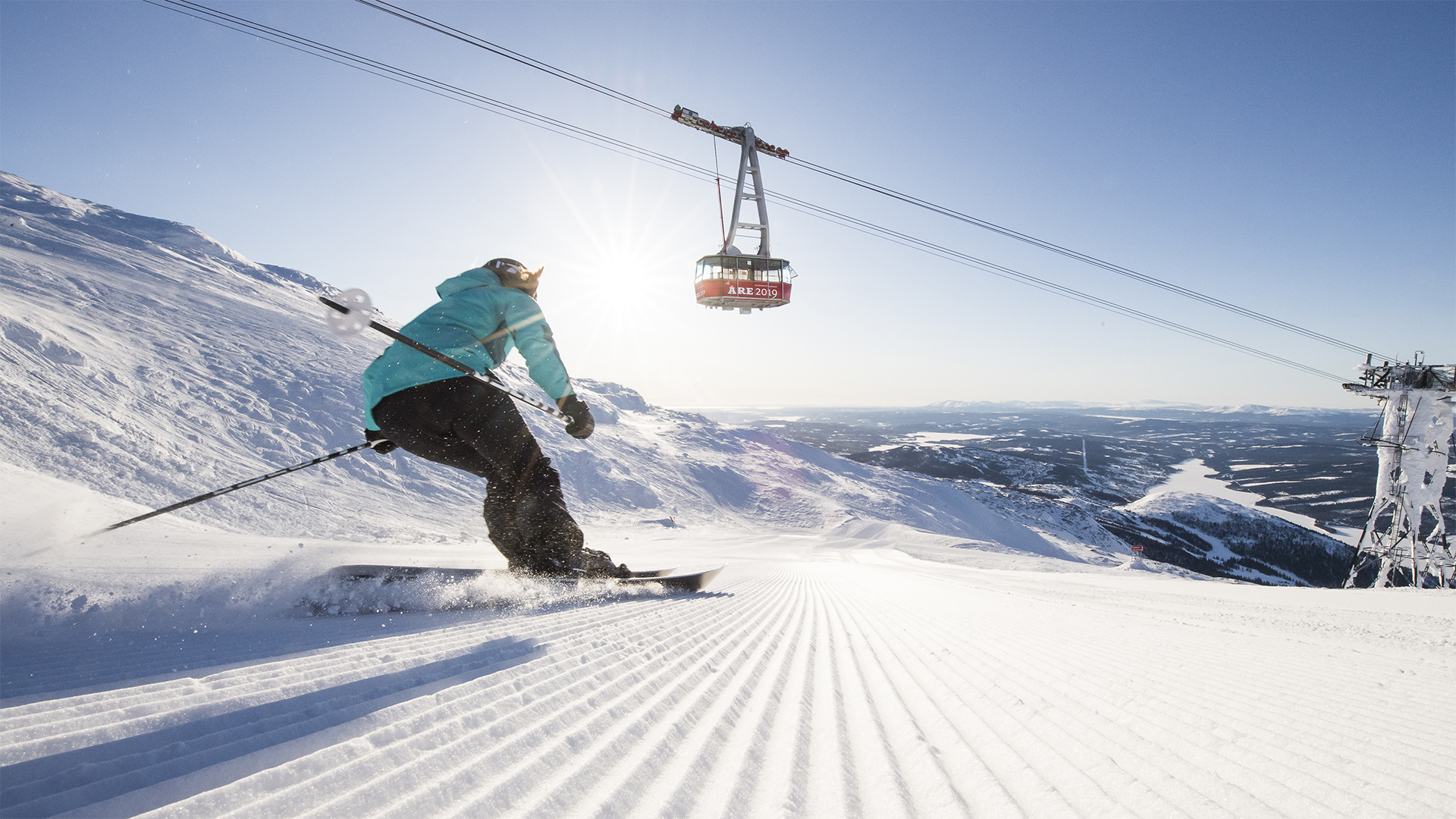 Skidåkare nedför pist i Åre med linbana i bakgrunden en solig dag