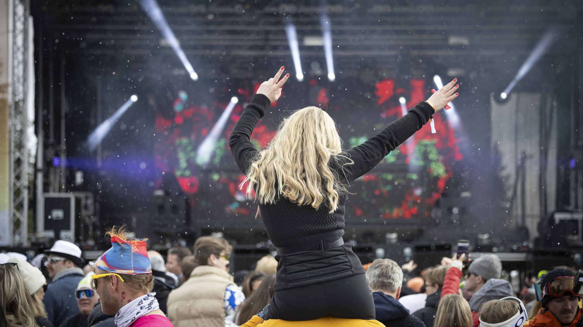 Konsertpublik med kvinna på axlar, som njuter av livemusik och ljusshow utomhus