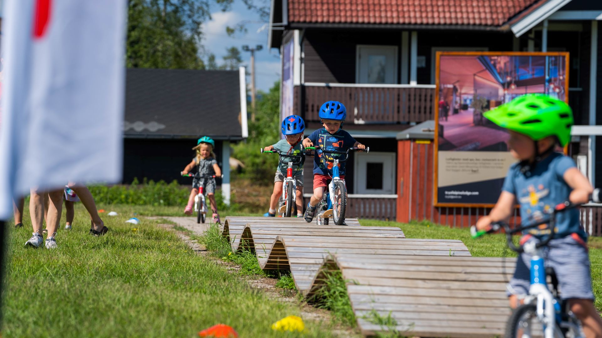 Barn med hjälm cyklar på träbanor i en cykelpark under sommaren