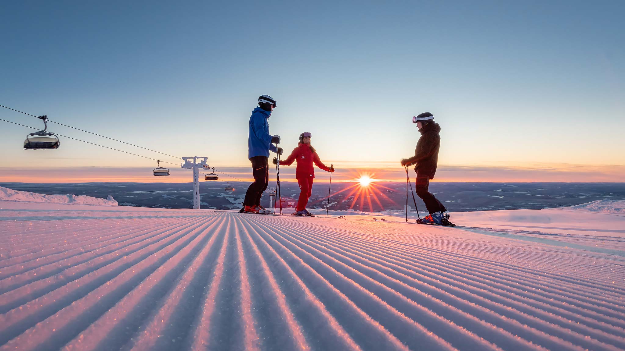 Skidåkare på snötäckta fjäll i solnedgången med kabinliftar i bakgrunden
