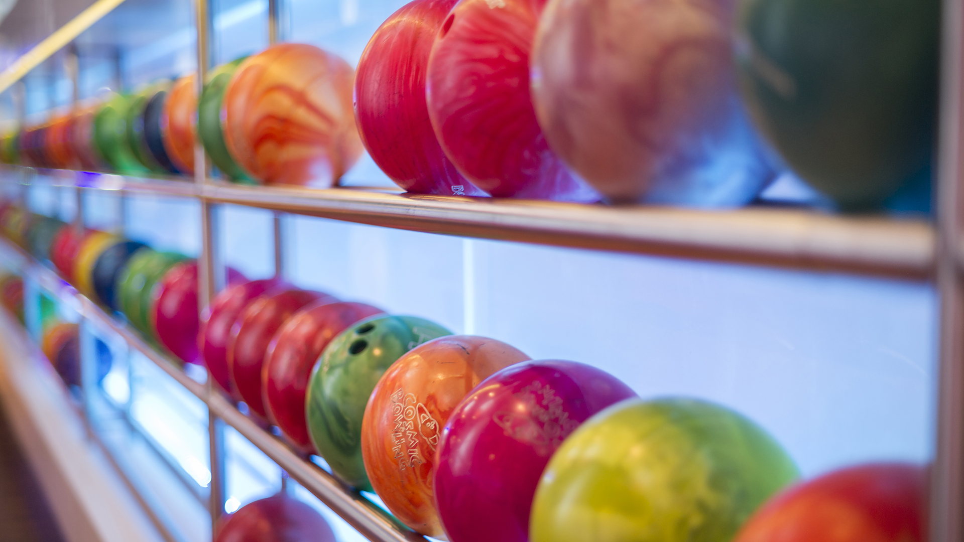 Färgglada bowlingklot på rad i en bowlinghall, med ledstång i förgrunden
