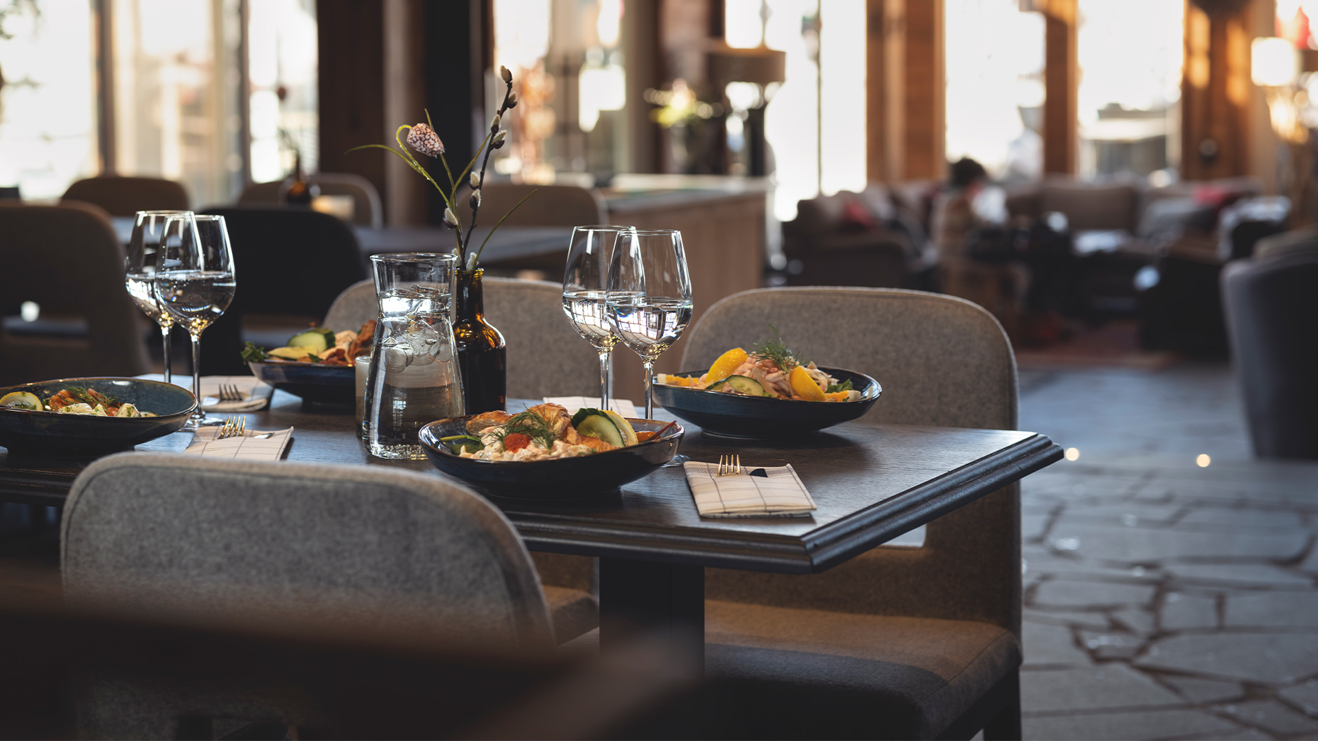 Restauranginteriör med elegant dukat bord, mat i skålar och vin i glas, mysig atmosfär med ljus genom fönstren