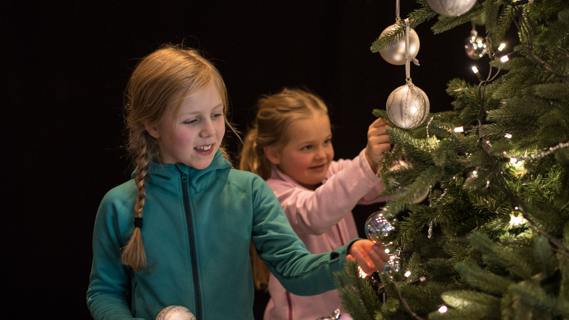 Två barn dekorerar en julgran med glittrande kulor och ljus
