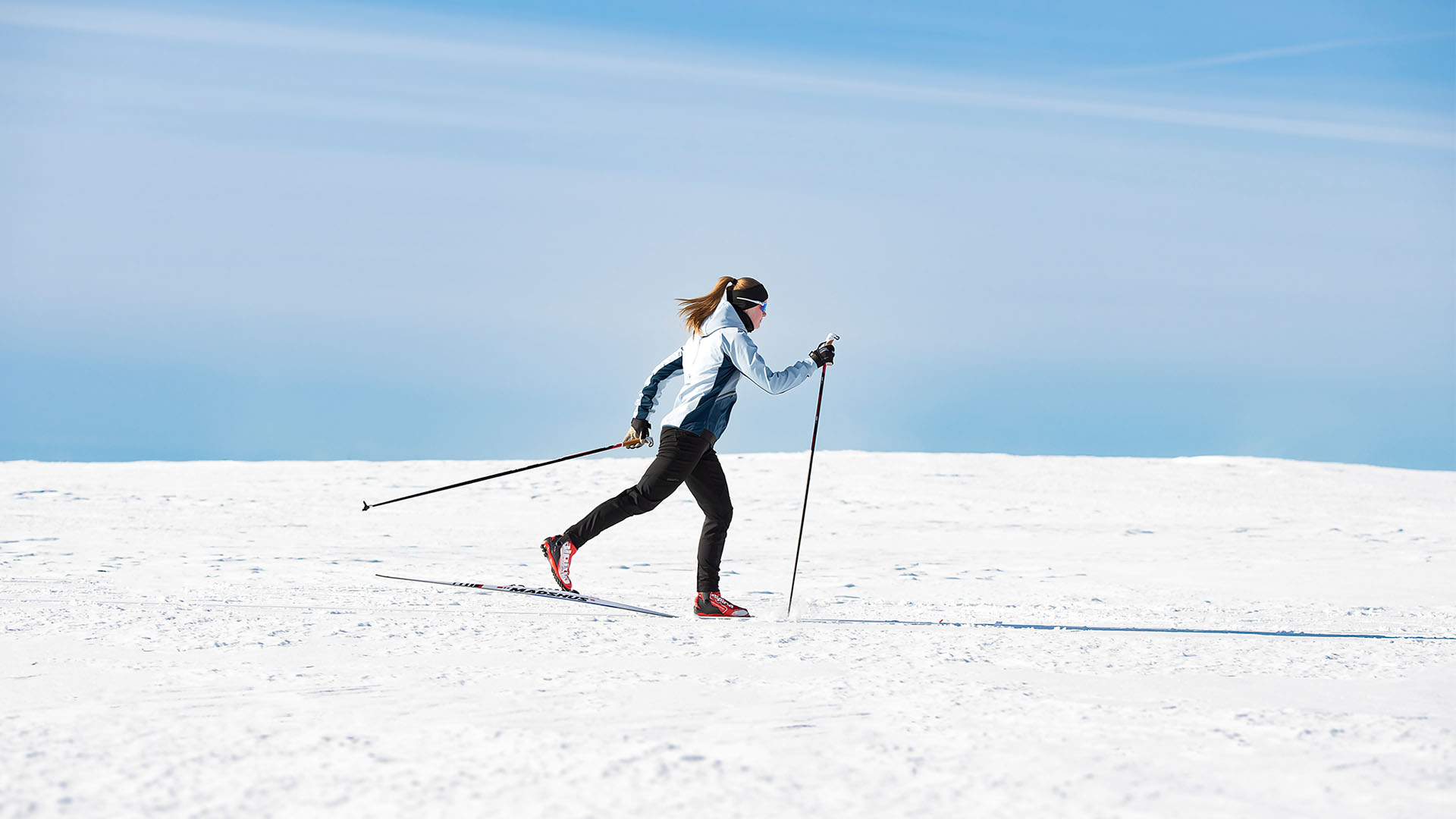 A person skiing with poles on a snow-covered landscape under a clear blue sky