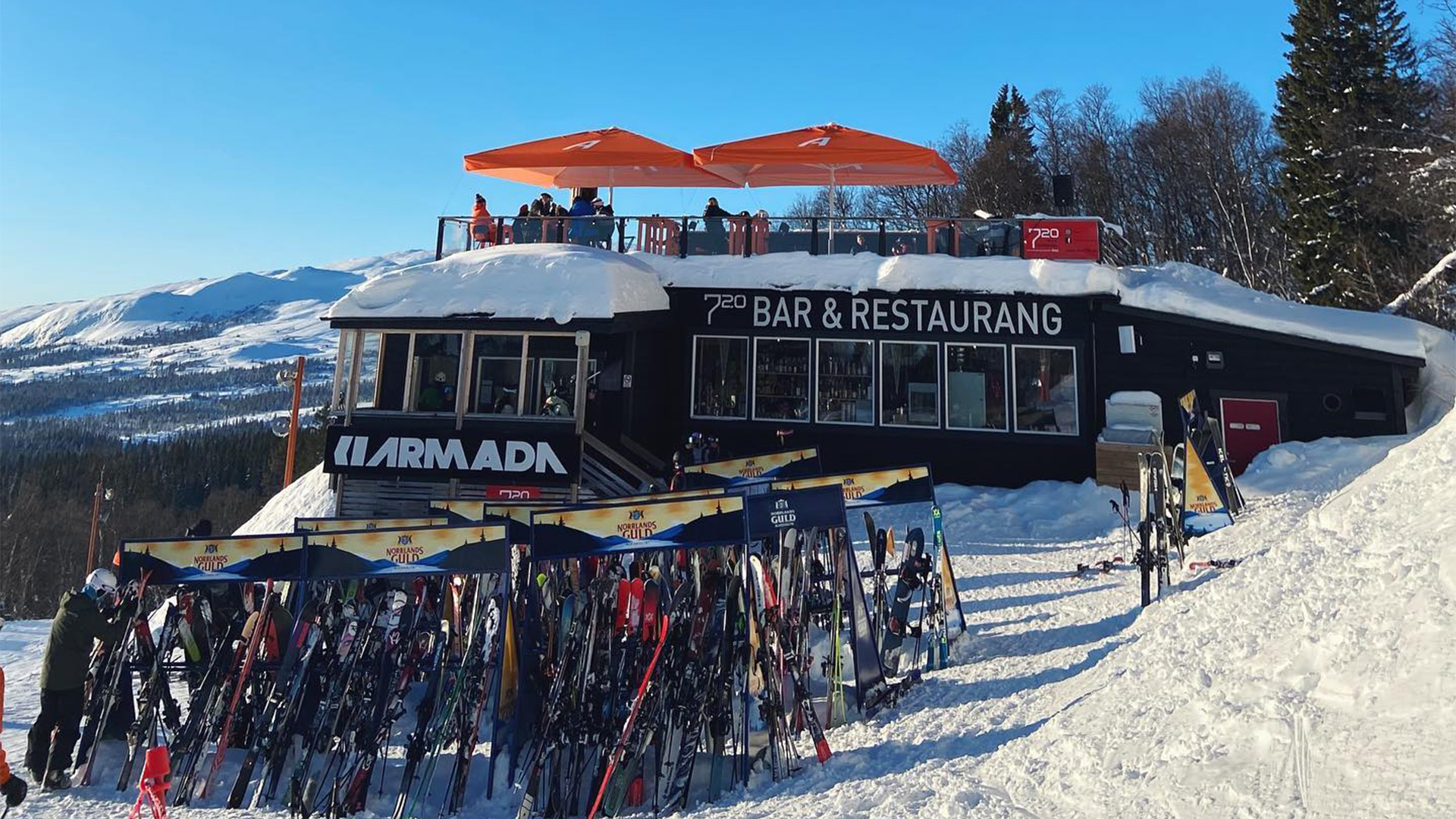 Skidrestaurang på fjällsluttning med skidor parkerade utanför; snöig miljö och klart väder
