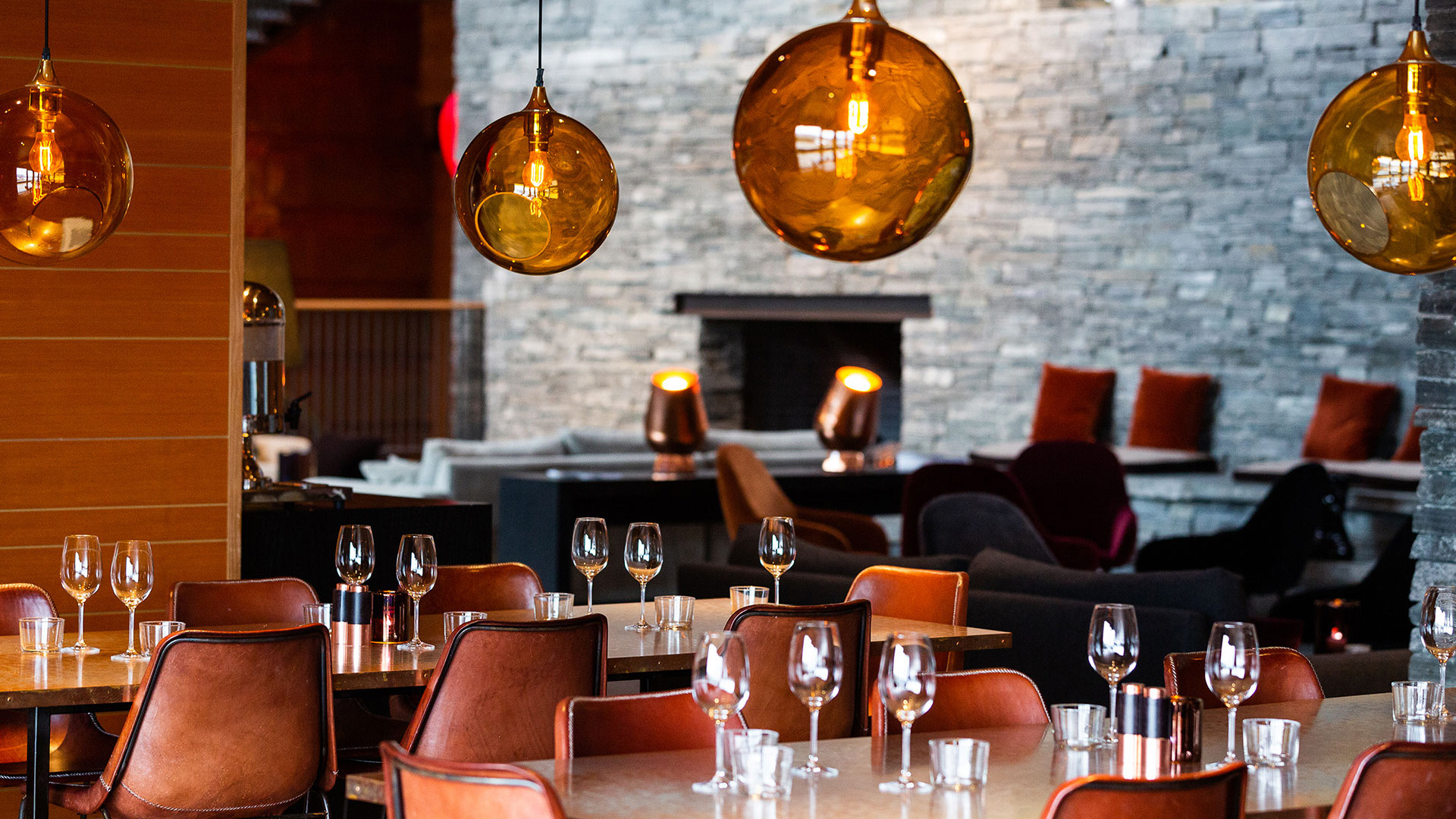 Restauranginteriör med eleganta bruna stolar, dukade bord och varma glaskupor som belysning, mot en stenväggsbakgrund