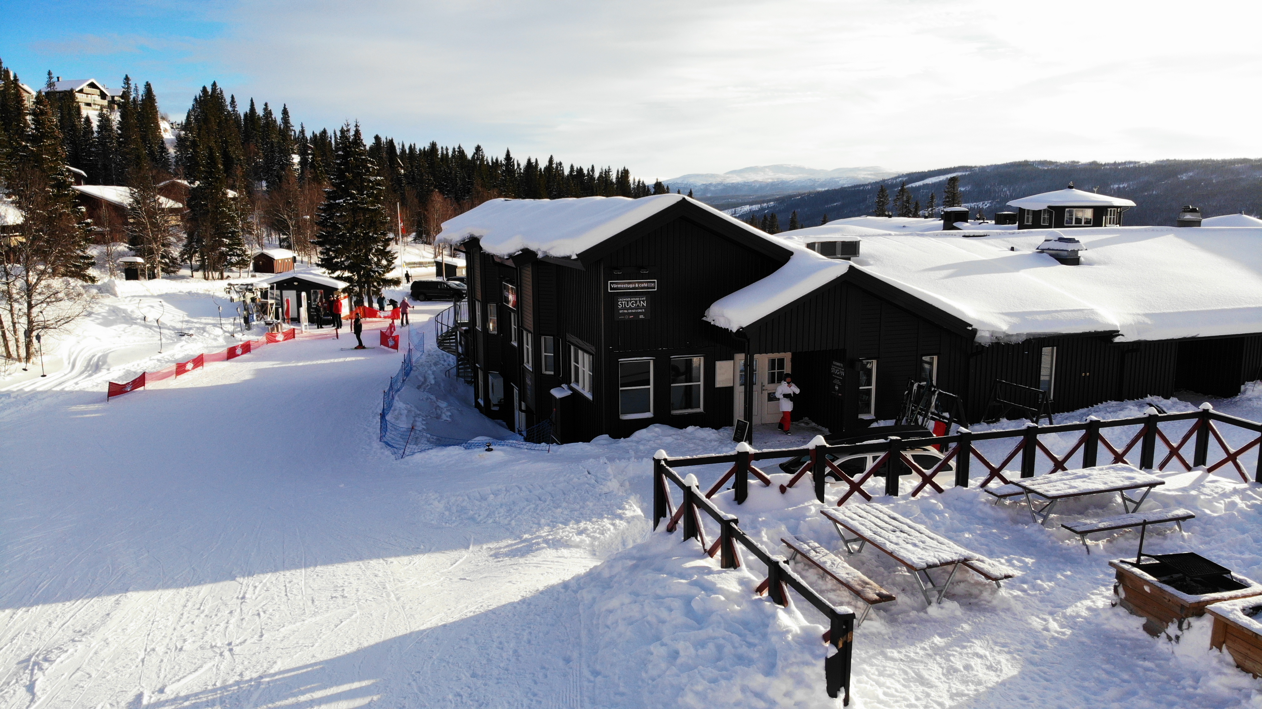Snötäckt fjällstuga vid skidbacke i soligt vinterlandskap med skog i bakgrunden i Sverige