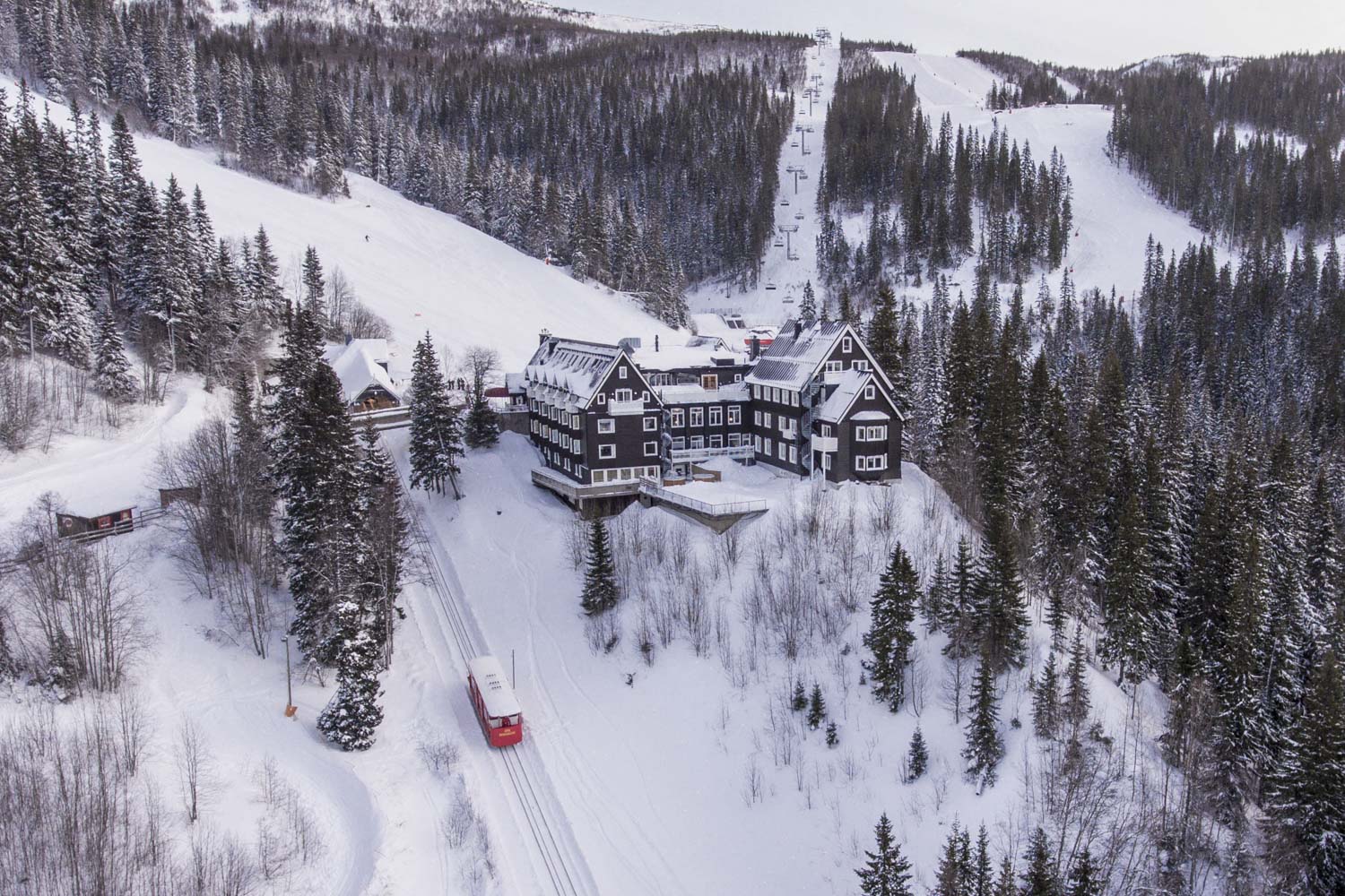 Vinterlandskap i Åre, Sverige med snötäckta skogar, bergssluttningar och en klassisk fjällstuga omgiven av snö. En tåg räls syns nära stugan