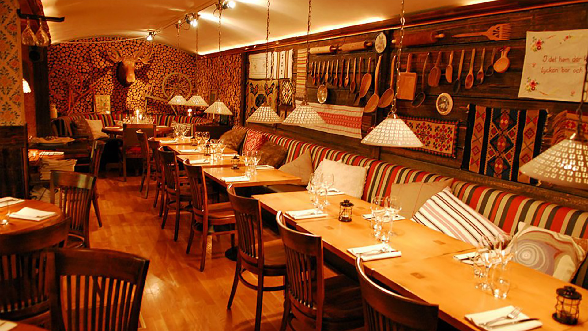 Traditionell svensk restauranginteriör med träbord, stolar och dekorationer, inklusive horn på väggen samt mönstrade textilier
