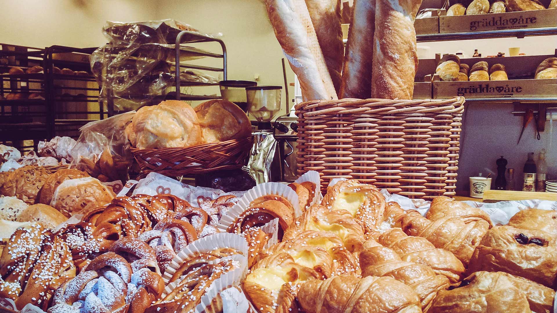 Ett urval av nybakat bröd och bakverk i ett traditionellt svenskt bageri, inklusive baguetter, bullar och croissanter i en korg och på en hylla
