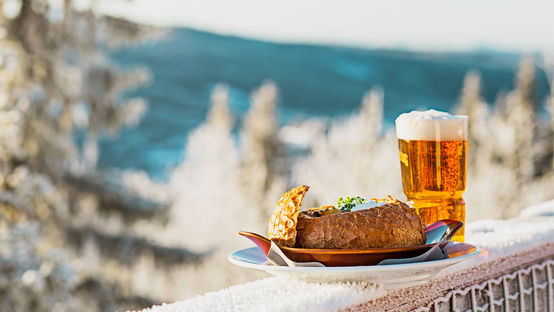 Fylld brödbulle med soppa och glas öl på terrassbord, vinterlandskap i bakgrunden