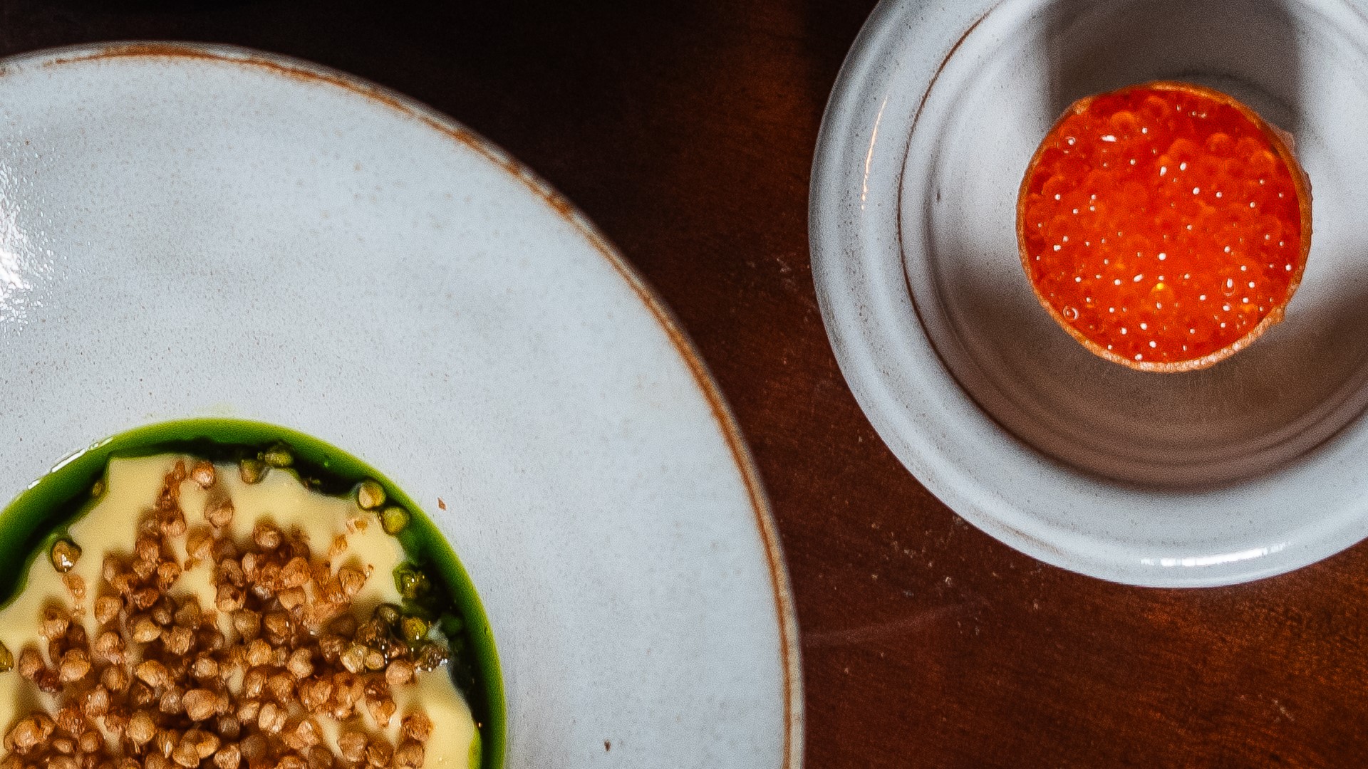 Tallrik med krämig rätt toppad med knaprig textur och en skål med röd caviar på ett träbord